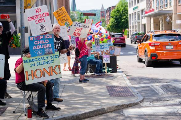 Numerous people fill a sidewalk and carry signs like "No concentration camps", "Stop ICE child Abuse", "Democracy Dies in Silence. Honk!"