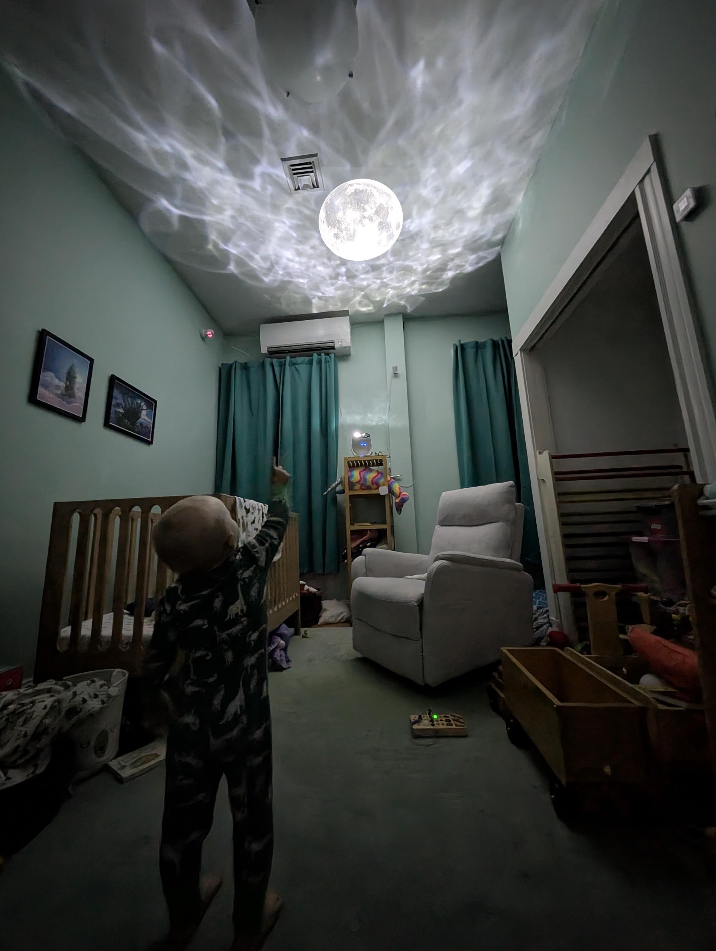 My kid, pointing up at his bedroom ceiling where there's a picture of the moon being projected, surrounded by galaxy projector caustics.