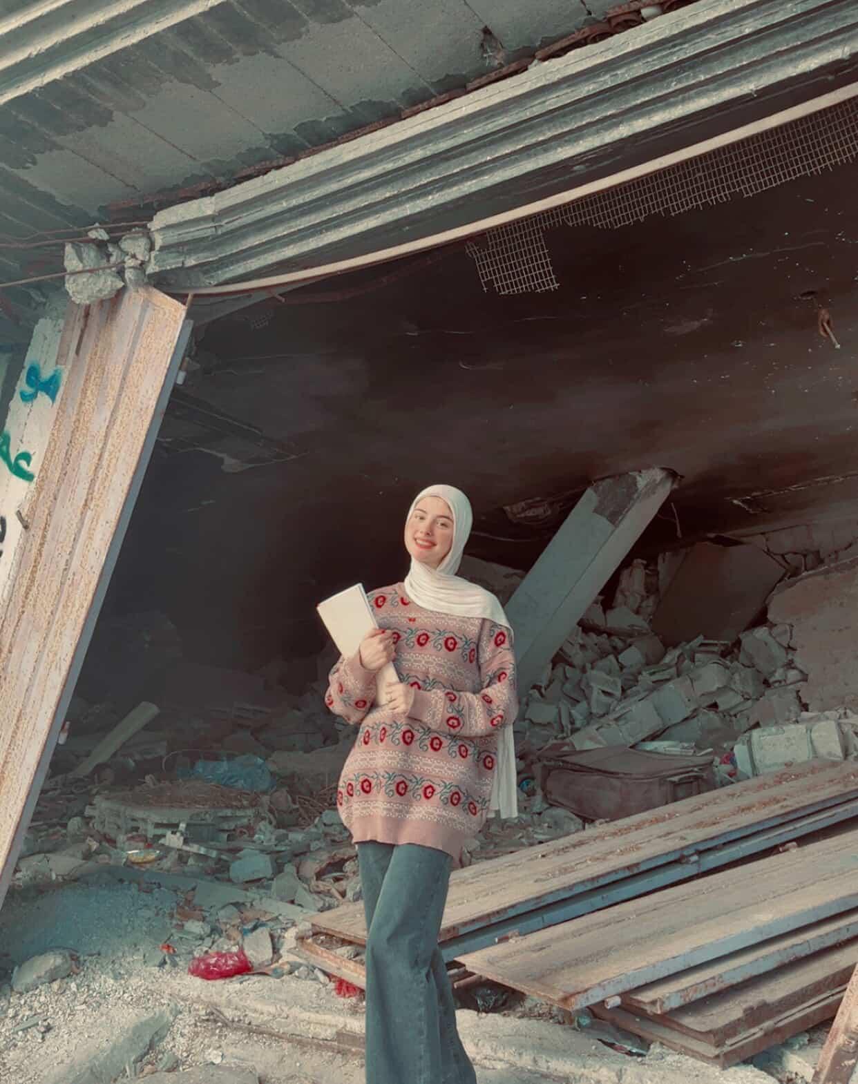 A girl with a book in front of a destroyed house in Gaza