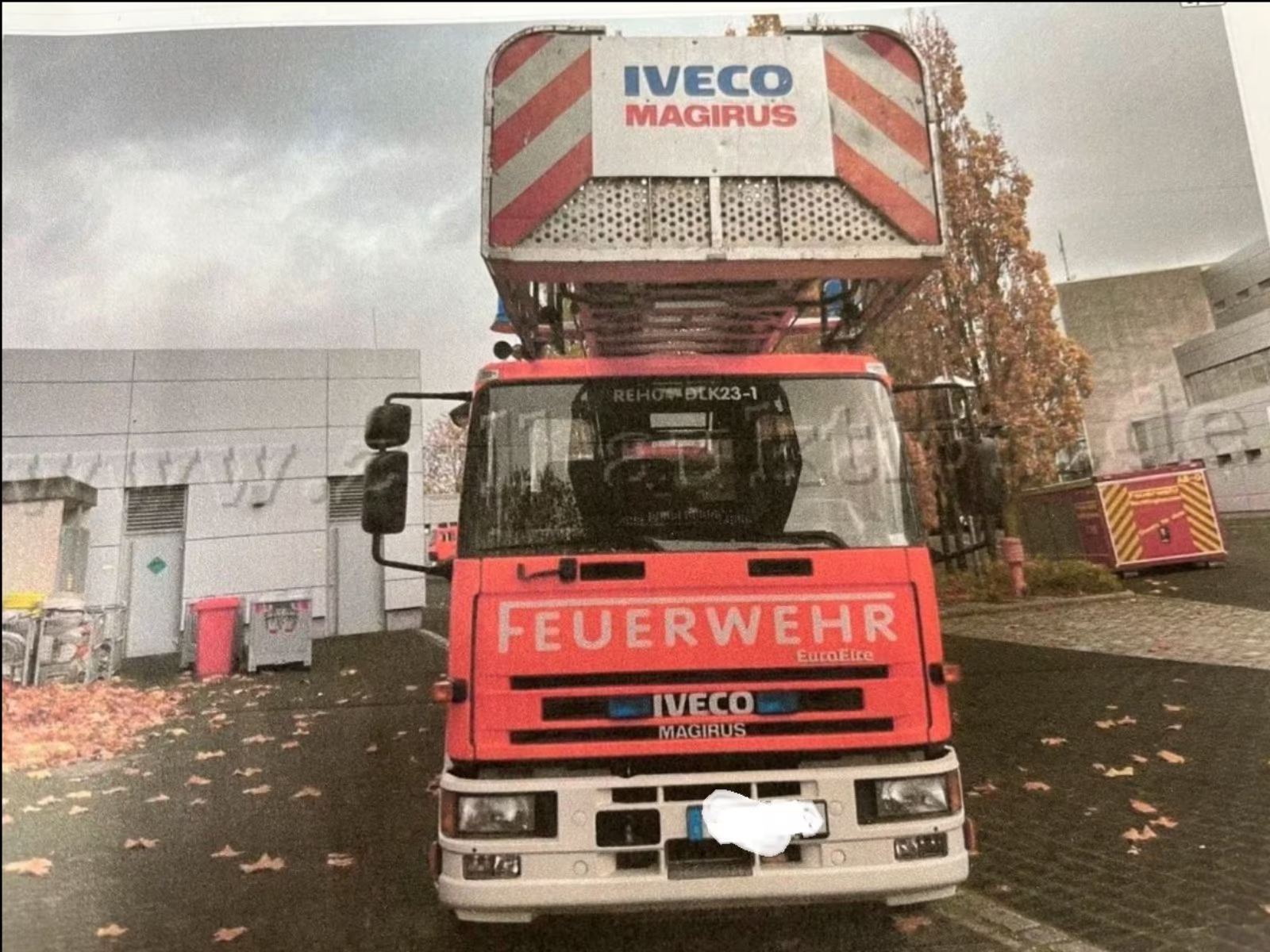 Frontalansicht eines roten Feuerwehr LKW mit Drehleiteraufbau vor grauen Hallentoren