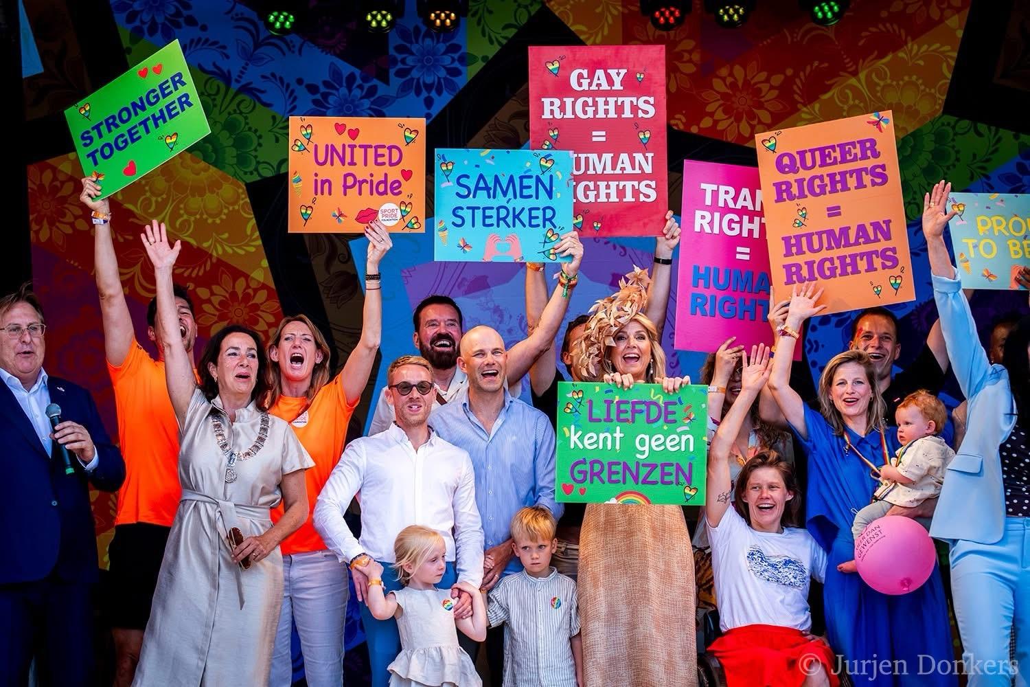 Queen Maxima in a crowd holding signs in support of the LGBTQ+ community. The queen has a sign that says "Liefde kent geen grenzen" -- in English, "Love knows no borders."
