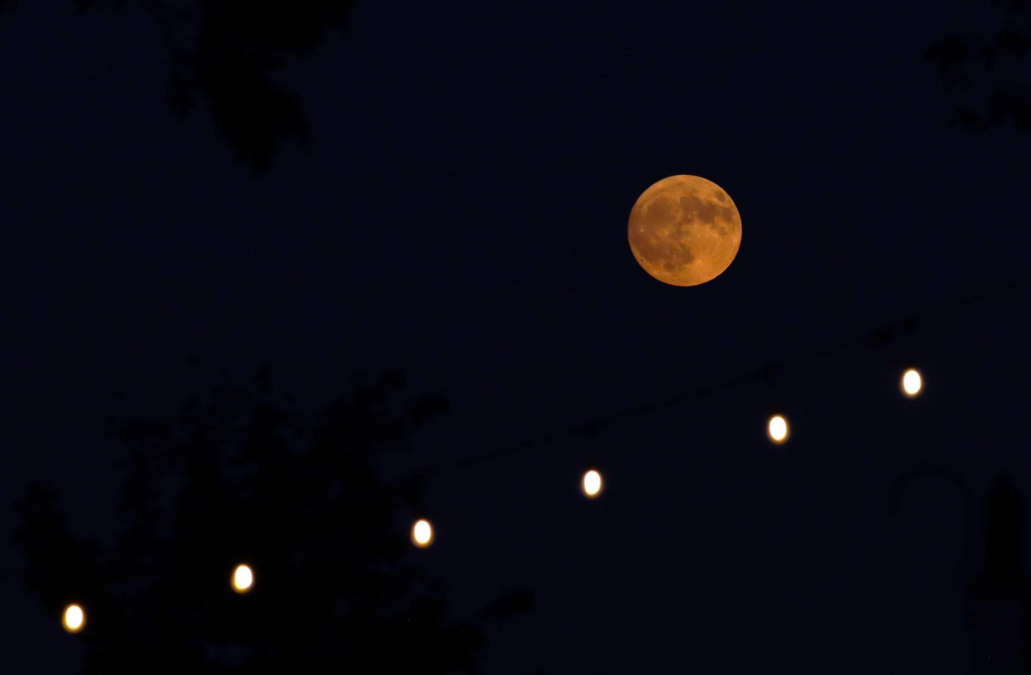 Photograph of a full Moon rising over a string of white lights.