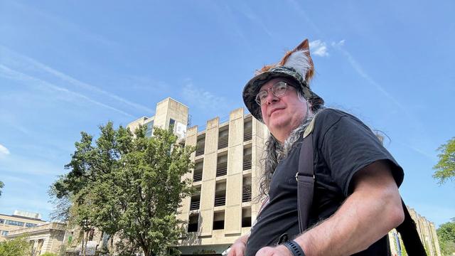 That guy wears a boonie cap with fox ears to smile when he does street photography but he's got a wry look on his face instead because behind him a concrete parking garage looms and that parking garage is permanently closed due to structural problems