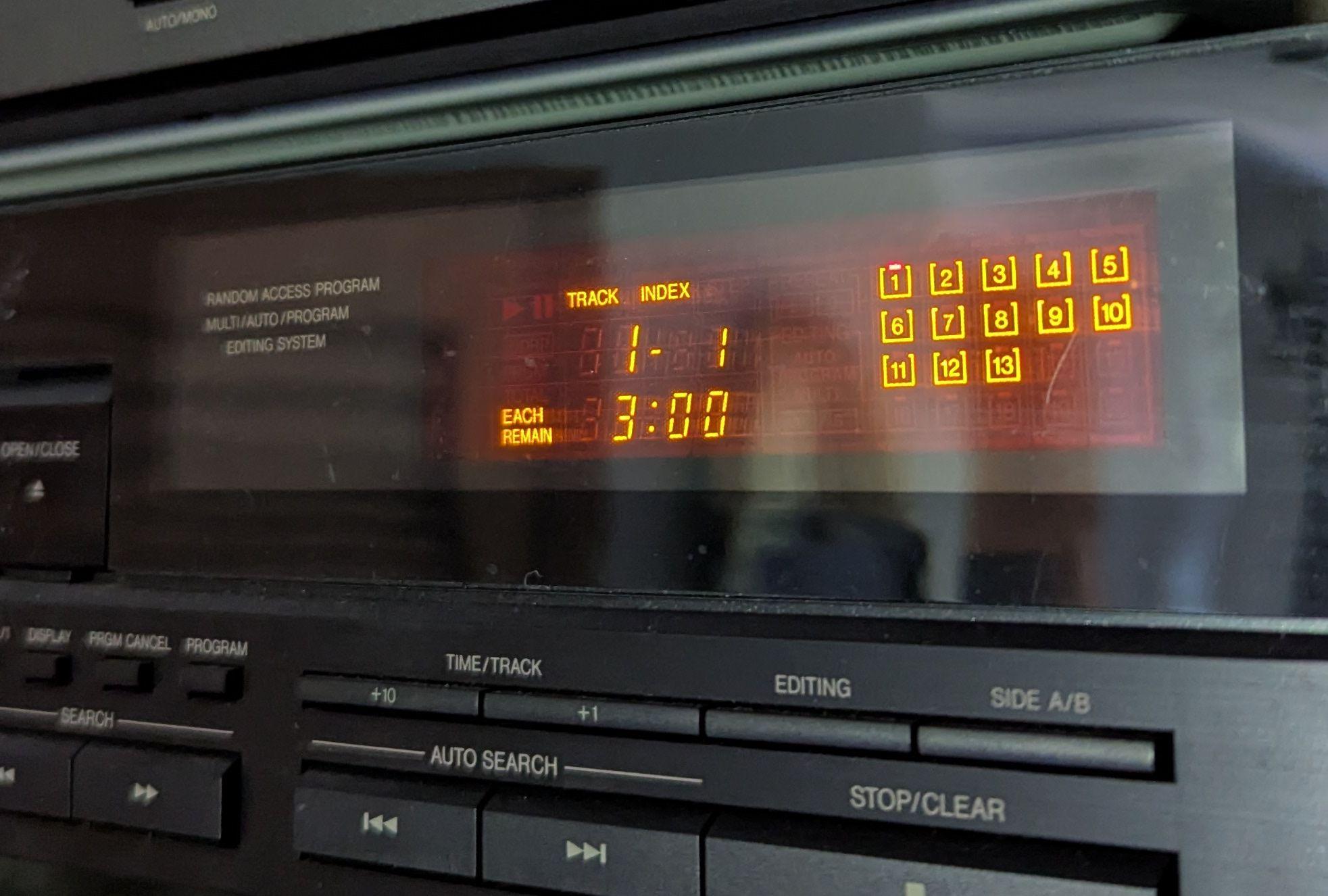 A photograph of the orange vacuum fluorescent display of a CD player in a stereo dual. The display of currently indicating that track 1 of 13 is playing, and that there are 3 minutes left in the track.