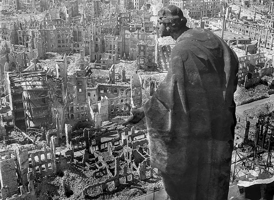The destruction of Dresden visible from its Rathaus ('townhall') in 1945. The view is from on high and looks past an undamaged angelic statue which appears to be surveying the ravaged and desolate landscape of burned out buildings below.