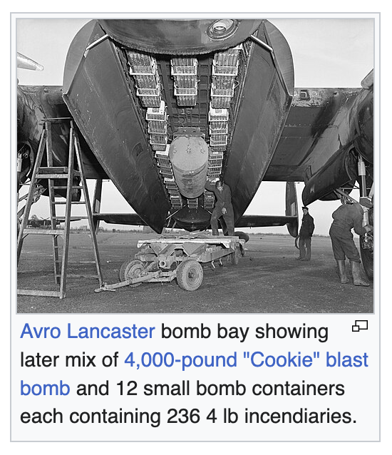 View from beneath a grounded Avro Lancaster, showing its bomb bay with a later mix of 4,000-pound ‘Cookie’ blast bomb and 12 small bomb containers each containing 236 4 lb (1.8 kg) incendiaries. Some men are working on loading it.