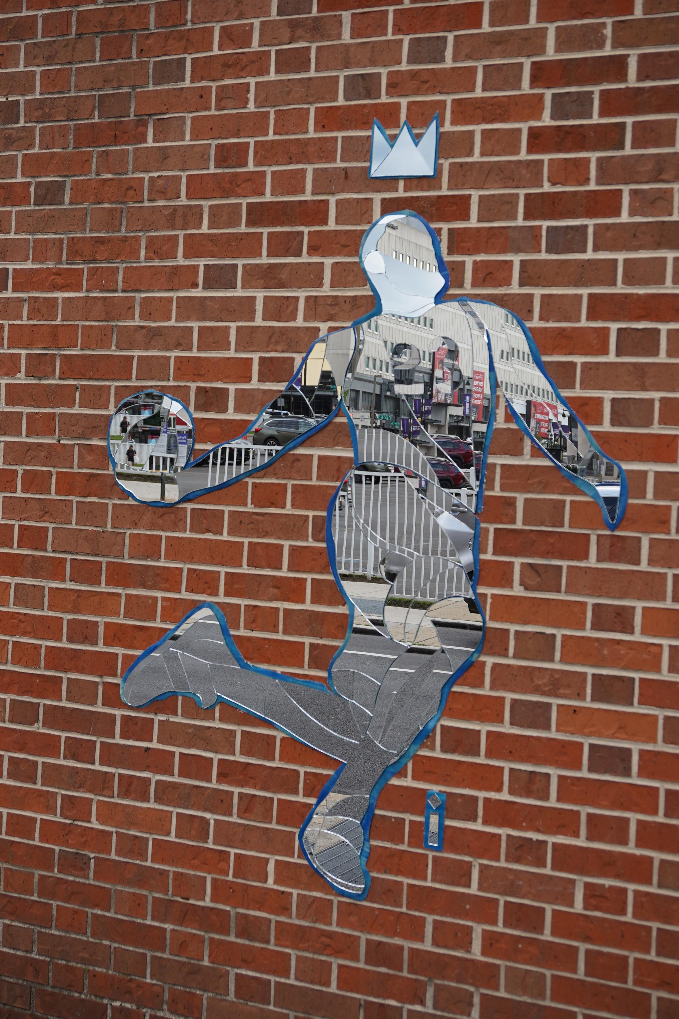 A mosaic of mirror pieces posted on a brick wall. The mirror pieces together depict LeBron James getting ready to dunk a basketball with a crown over his head.