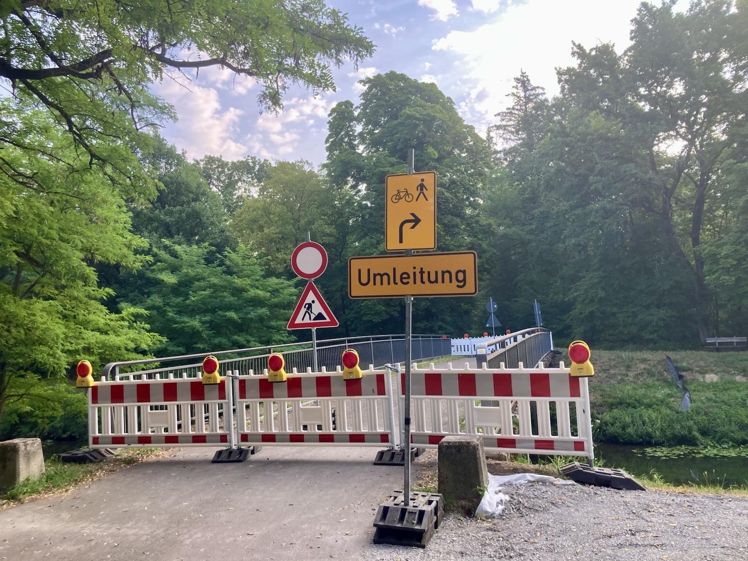 A blocked pathway over a bridge -Traffic signs indicate a detour for bicycles and pedestrians along the water…