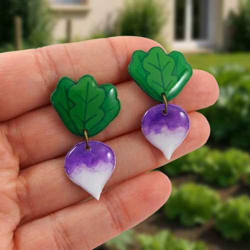 Puces d'oreilles fantaisie pendantes éco-responsables en forme de navets blancs et violets, et ses feuilles.
Les parties "feuilles" sont fixées aux oreilles grâce à des clous d'oreilles en acier inoxydable (vous pouvez également choisir des clips pour les oreilles non percées), et les navets y sont rattachés avec un anneau de couleur bronze.
Les perles sont réalisées en CD/DVD recyclé, découpées et peintes à la main, puis recouvertes de résine.
Ces puces d'oreilles sont tenues entre les doigts tendus d'une main ouverte devant un fond violet pastel.
