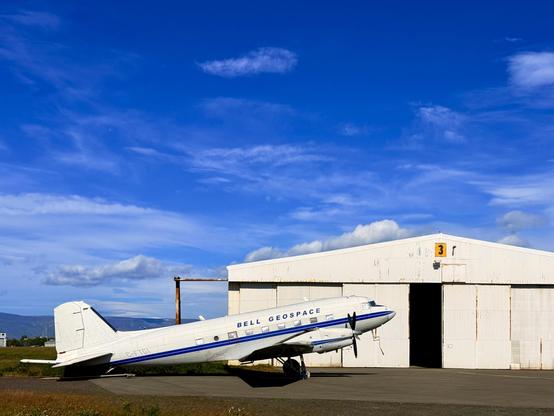 A converted DC-3 aircraft is parked in front of a hanger in Reykjavík. The sky is very blue. 