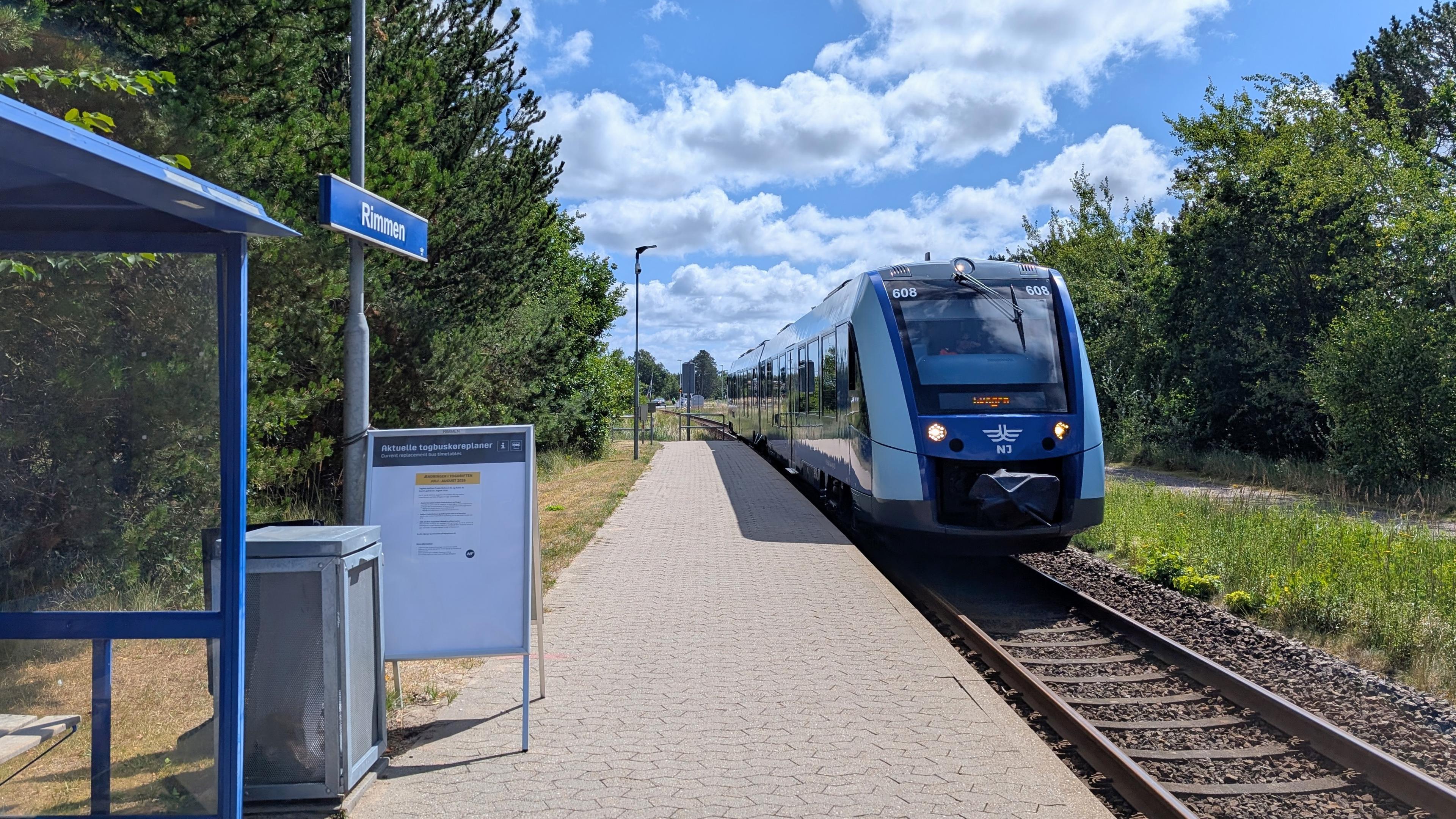 A train stop with a tiled platform and a small shelter, sign "Rimmen", arriving NJ LINT 41 DMU