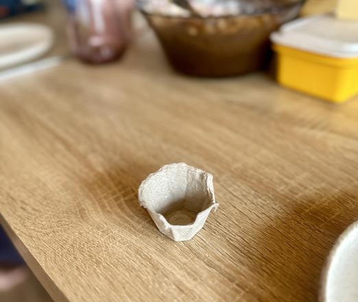 Holztisch, darauf ein sechstel Eierkarton als Becher.