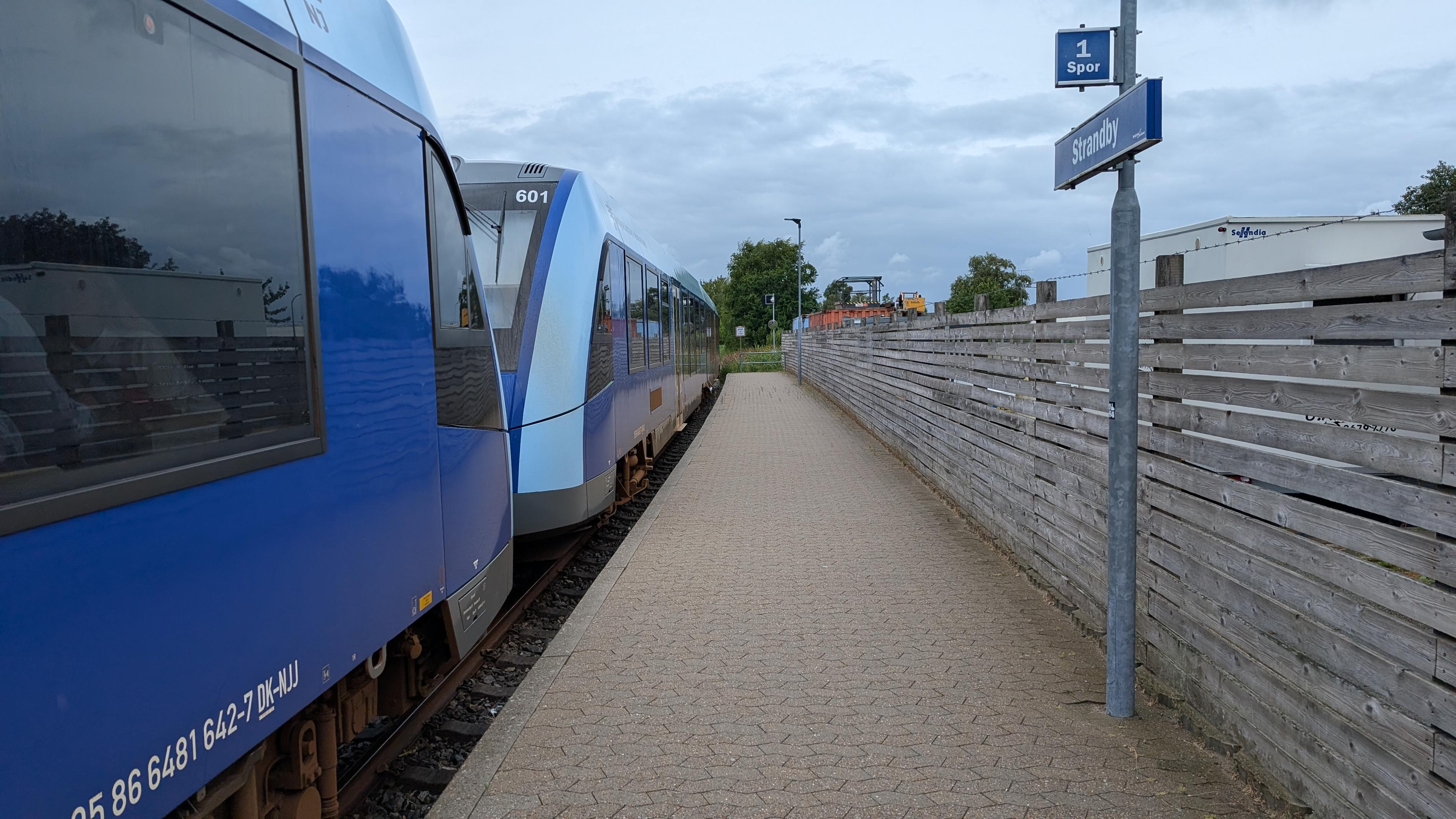 A train stop with a tiled platform and a sign "Strandby", two arriving NJ LINT 41 DMU sets at platform