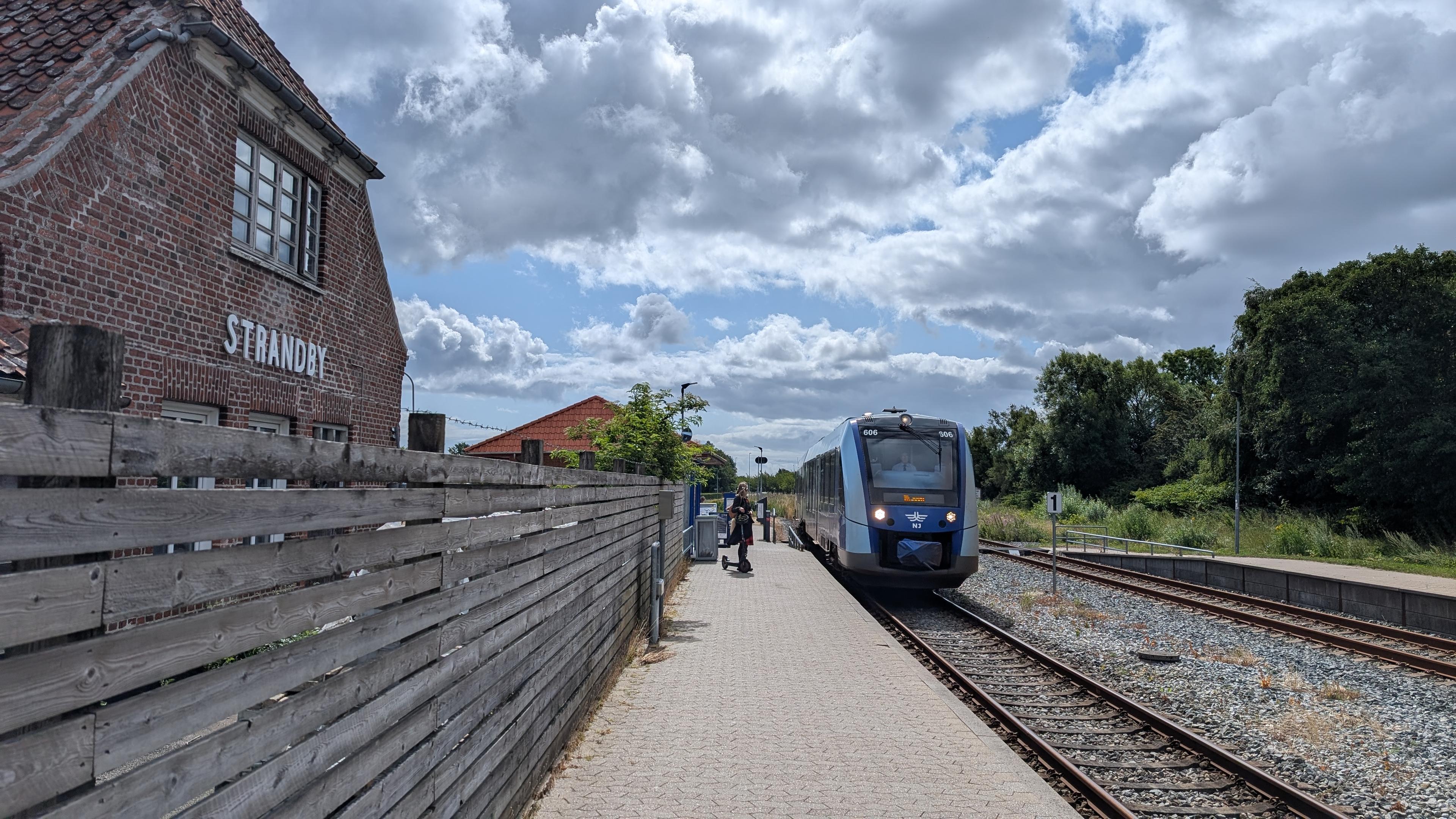 A NJ LINT 41 DMU at platform, a brick building on the other side of the platform behind a fence, white lettering 'Strandby'