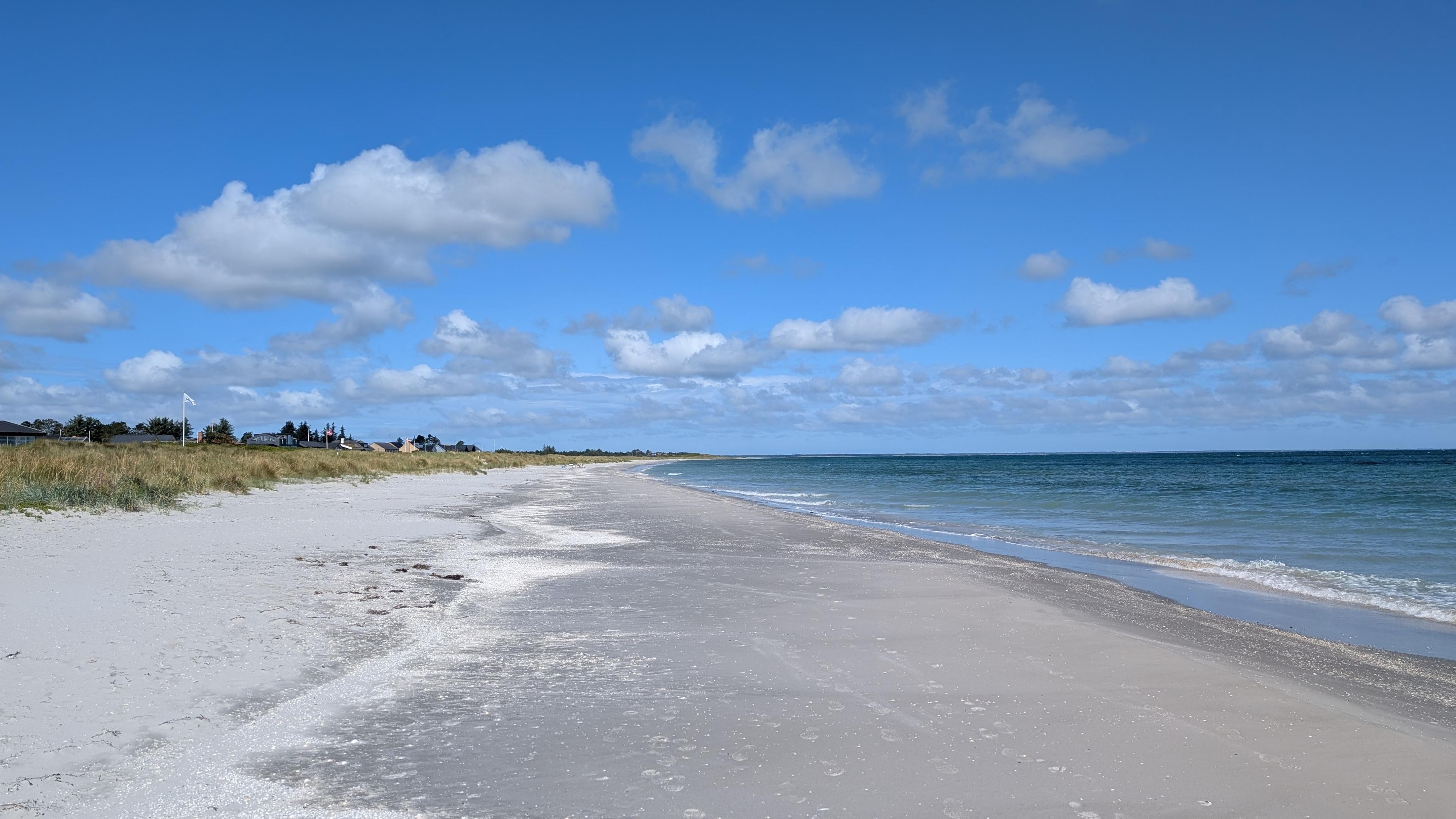 A flat sand beach, blue sky and sea, flat meadow and roofs of the houses