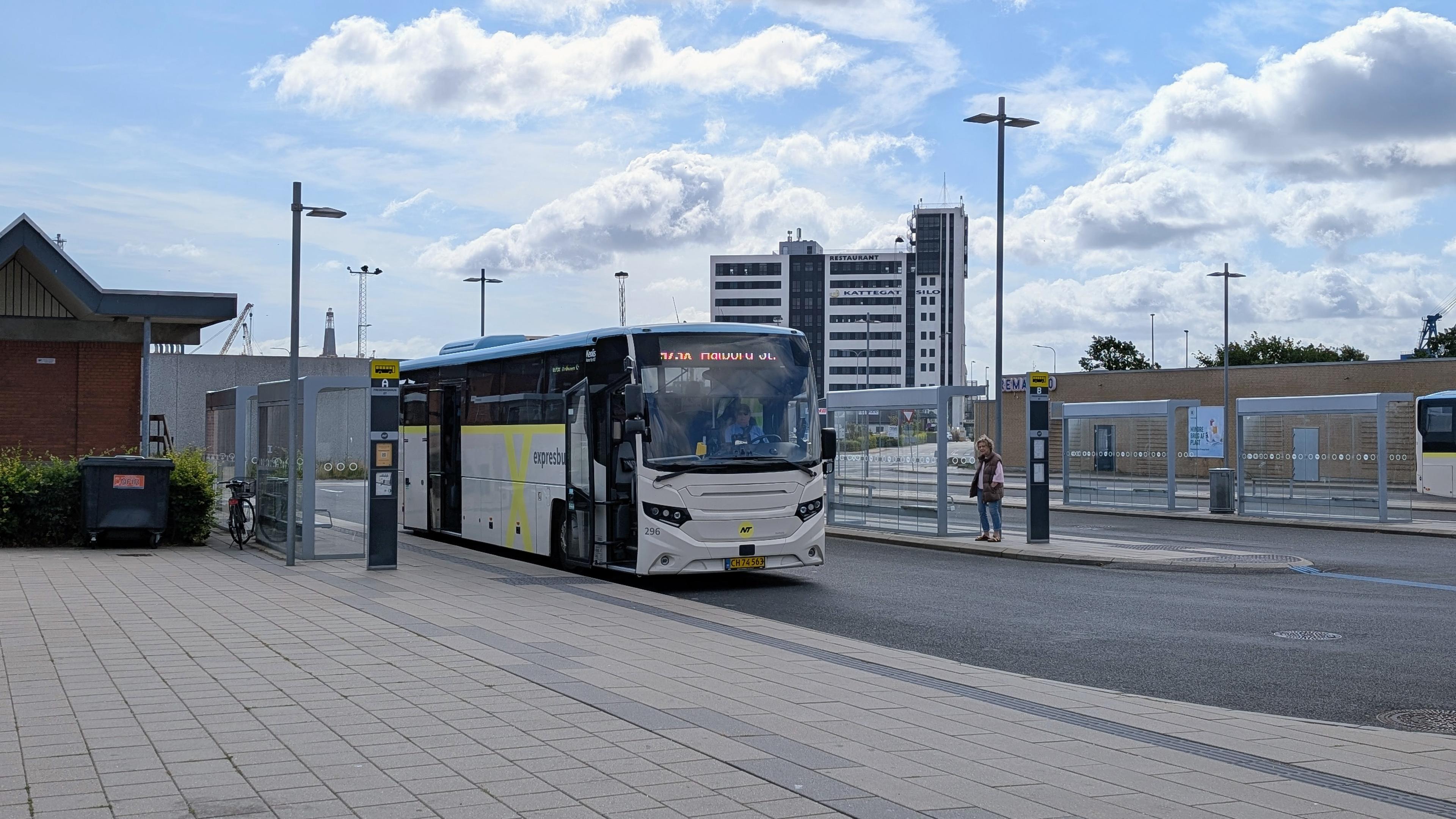 A high-floor bus with cream-blue NT livery, yellow X underneath the windows, destination indicator '975X Aalborg St.'