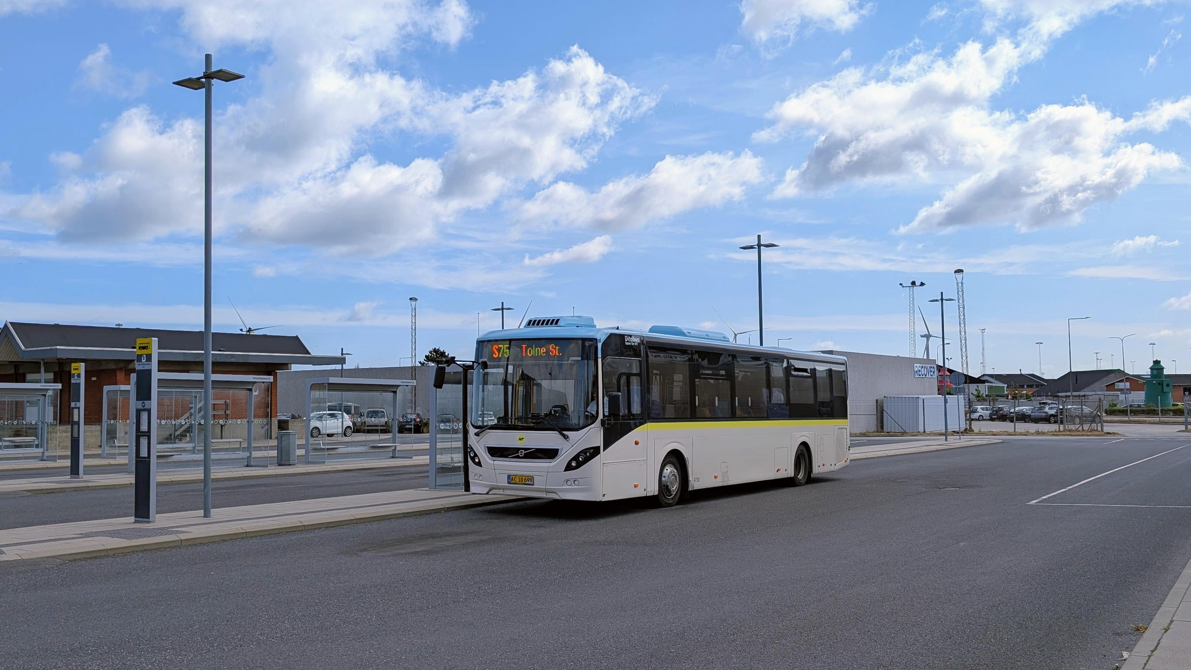 A high-floor bus with cream-blue NT livery, yellow X underneath the windows, destination indicator '975X Aalborg St.'