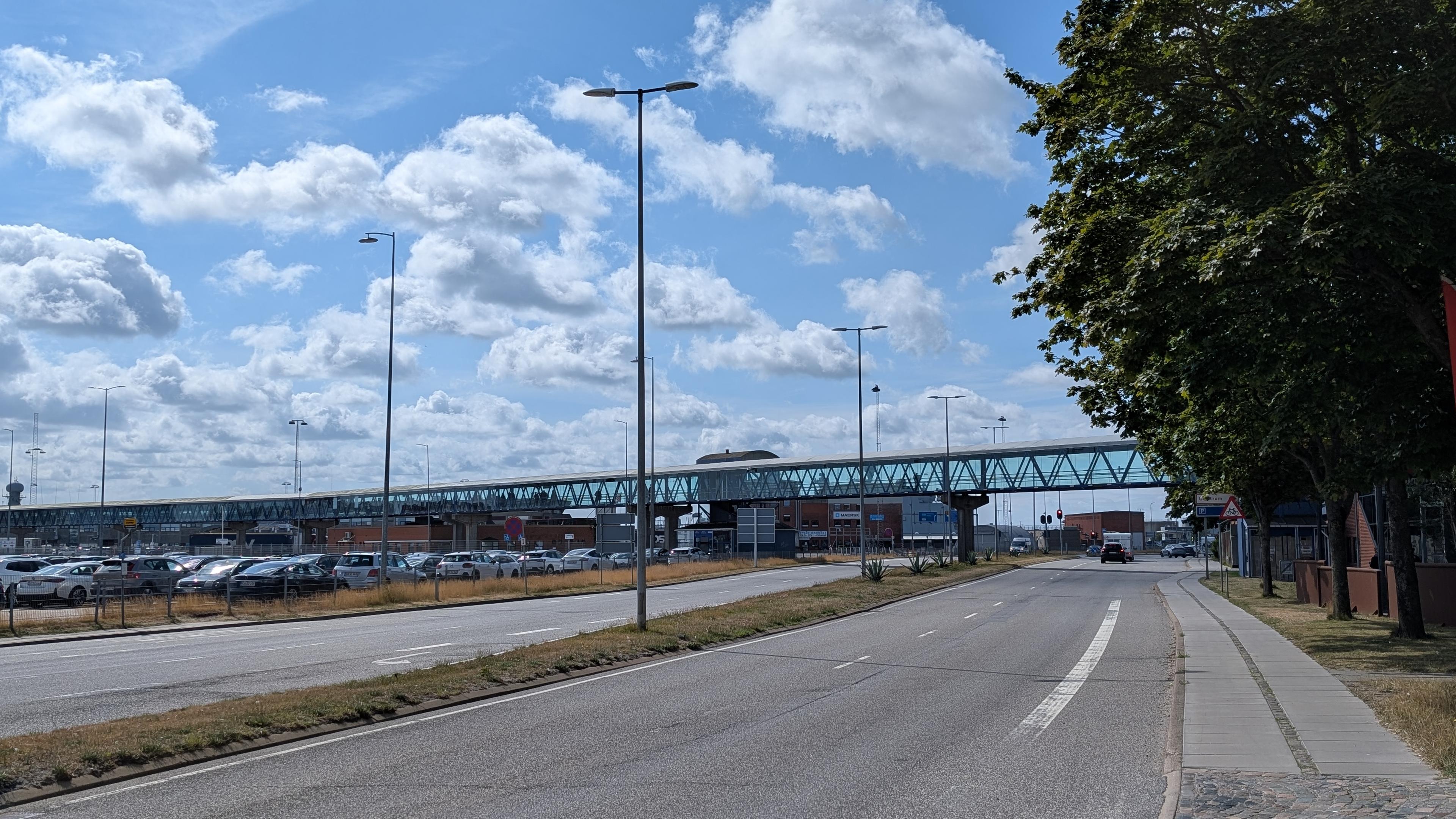 A covered pedestrian bridge with glass panes on both sides crossing a wide street and parking area
