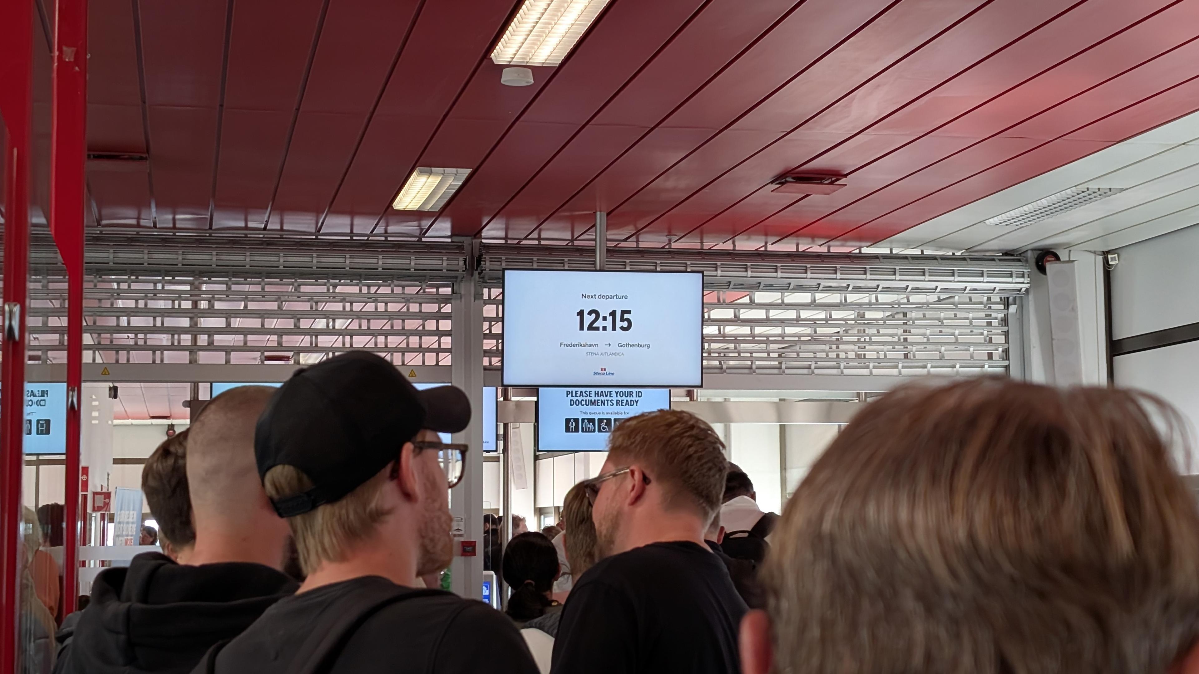 Heads of queueing people, a display with '12:15' in the background