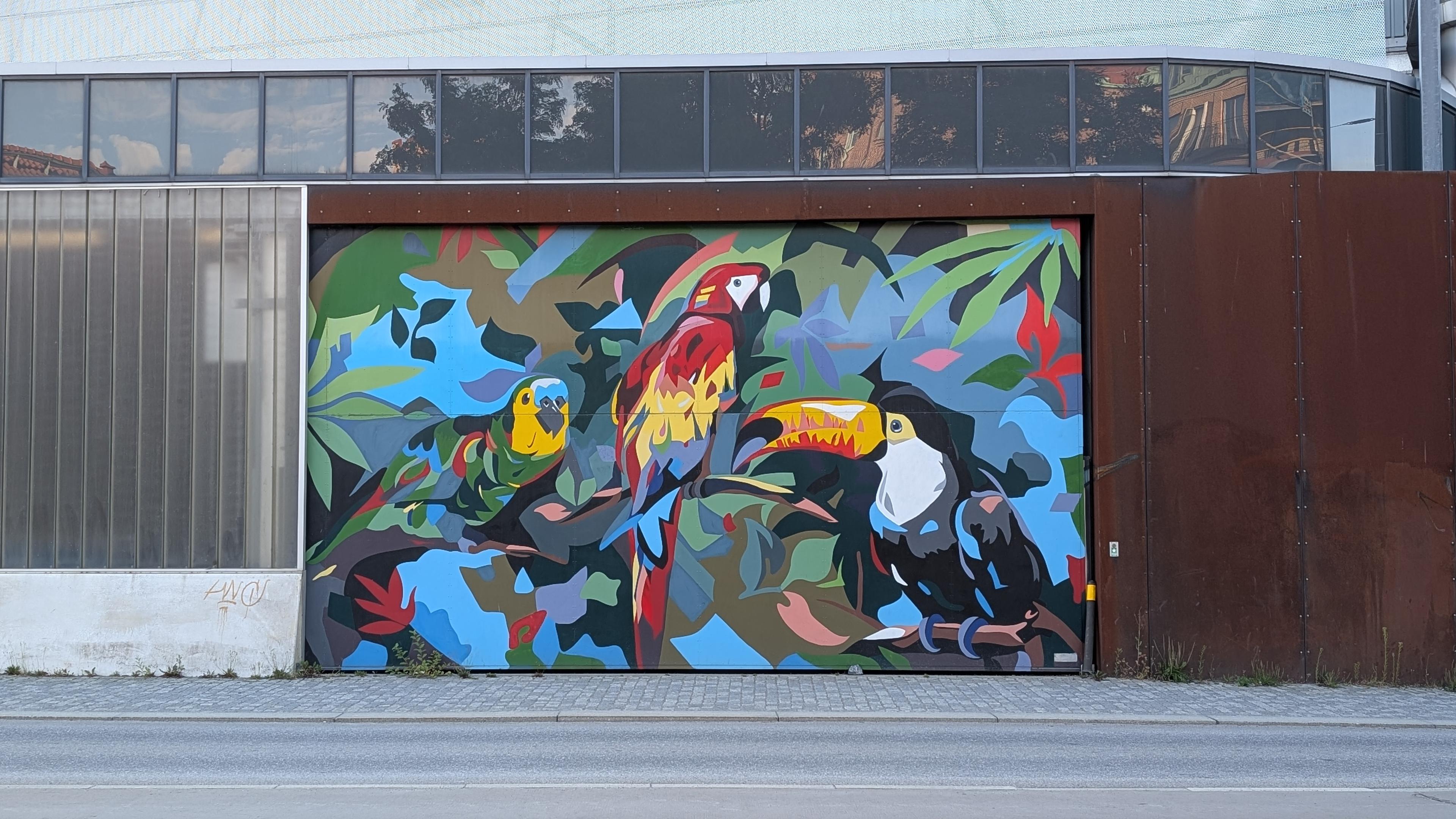 A door of an industrial building covered with street art, two parrots and a toucan on a branch