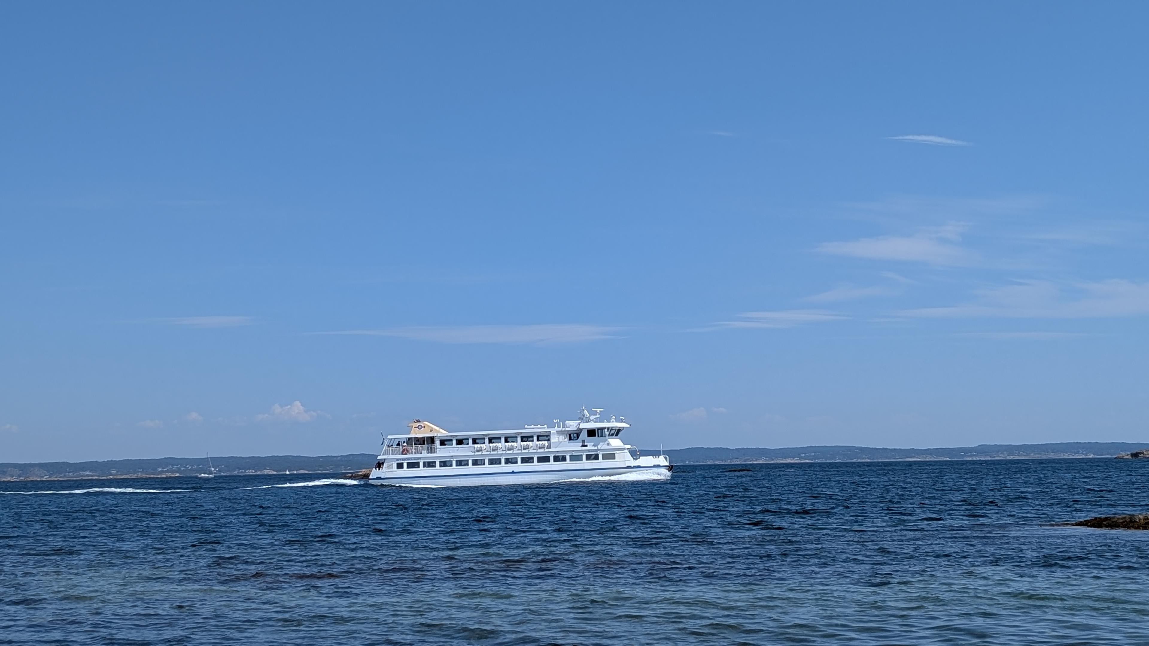 A double-deck boat driving from left to right in a deep-blue sea, blue sky