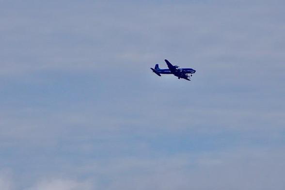 A blue and white airplane is flying through a cloudy sky above Reykjavík, Iceland.