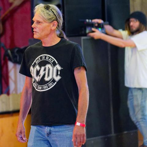 Man with greying hair has black shirt with a circular logo that says AC/DC Back in Black world Tour 1980-1981