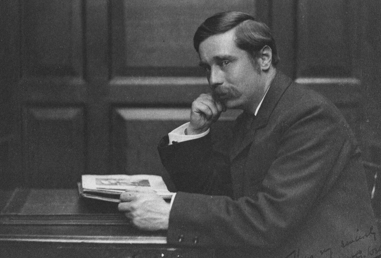 Black and white photograph c1890 of Author H.G. Wells seated looking at the audience his right hand to his face, his left on a book. Taken in the Library of the London School of Economics and Political Science.