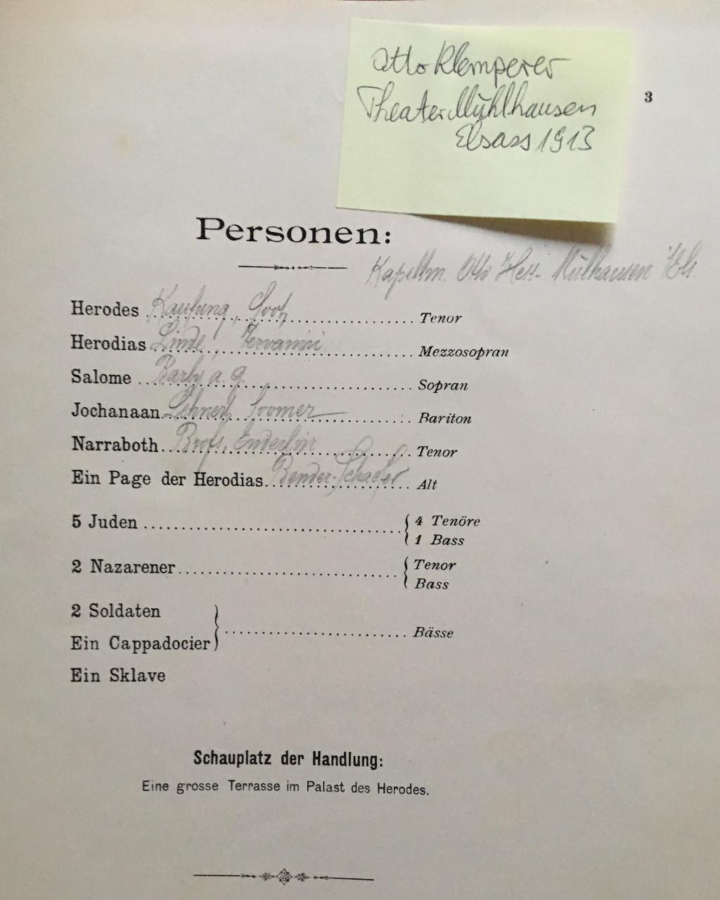 Yellowed page of an over 100 years old Salome vocal piano score with the role list and an attached post-it note. There are handwritten pencil notes between the role names and the voice types, presumably the surnames of the singers cast in the roles. The printed text reads, in German:

Personen:
Herodes … Tenor
Herodias … Mezzosopran
Salome … Sopran
Jochanaan … Bariton
Narraboth … Tenor
Ein Page der Herodias … Alt
5 Juden … 4 Tenöre 1 Bass
2 Nazarener … Tenor Bass
2 Soldaten
Ein Cappadocier … Bässe
Ein Sklave
Schauplatz der Handlung:
Eine grosse Terrasse im Palast des Herodes.

[Characters:
Herod … Tenor
Herodias … Mezzo-soprano
Salome … Soprano
Jochanaan … Baritone
Narraboth … Tenor
A Page of Herodias … Contralto
5 Jews … 4 Tenors, 1 Bass
2 Nazarenes … Tenor, Bass
2 Soldiers
A Cappadocian … Basses
A Slave
Setting:
A large terrace in Herod’s palace.]

The post-it note reads:
Otto Klemperer
Theater Mülhausen
Elsass 1913