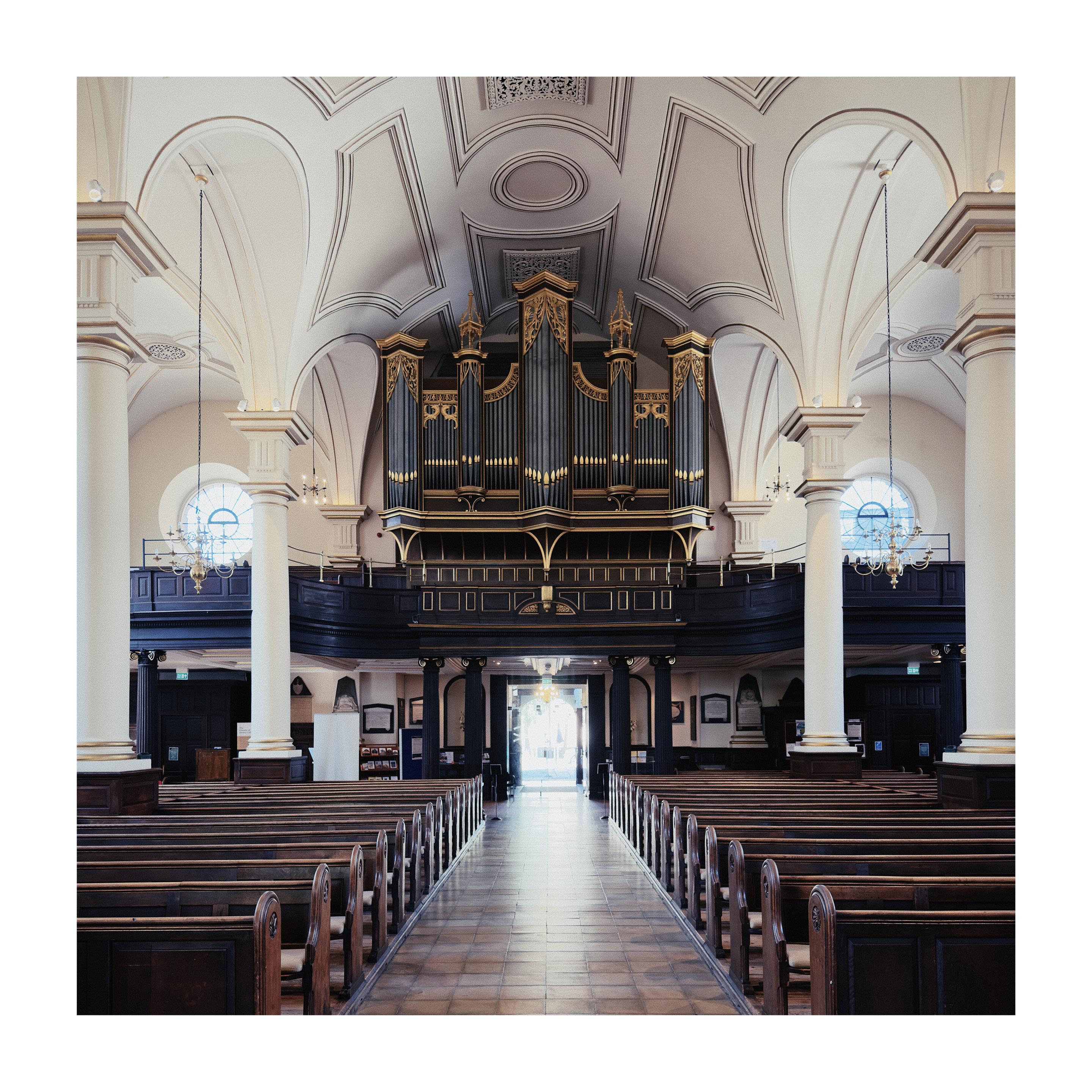 The interior of a symmetrical cathedral looking out towards the entrance/exit with a massive organ above the door.