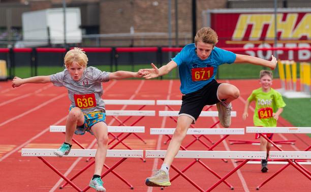 Two boys are flying over the hurdles near the center whereas a small boy on the right is approaching his first hurdle.
