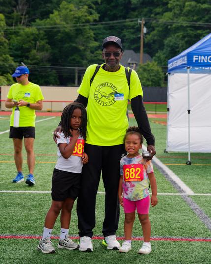 Black man poses with two black girld between FLRC tent and another volunteer in a yellow shirt