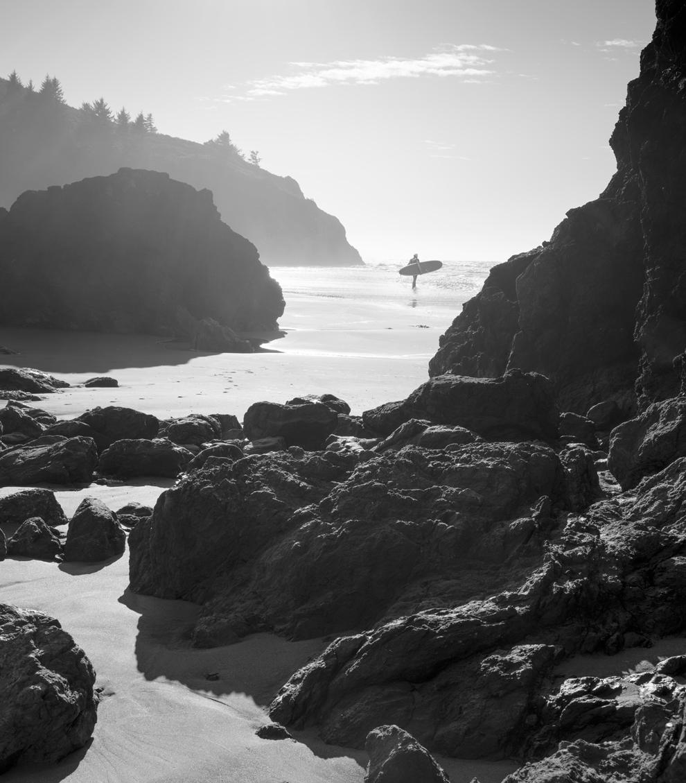 A black and white photograph of a surfer entering the ocean at Trinidad State Beach, California.
