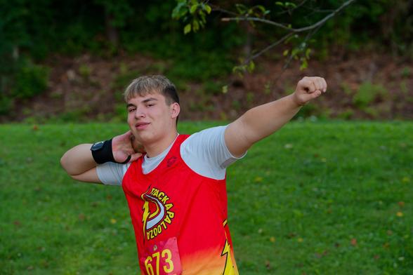 Men presses shot put ball into neck as he holds is other arm out