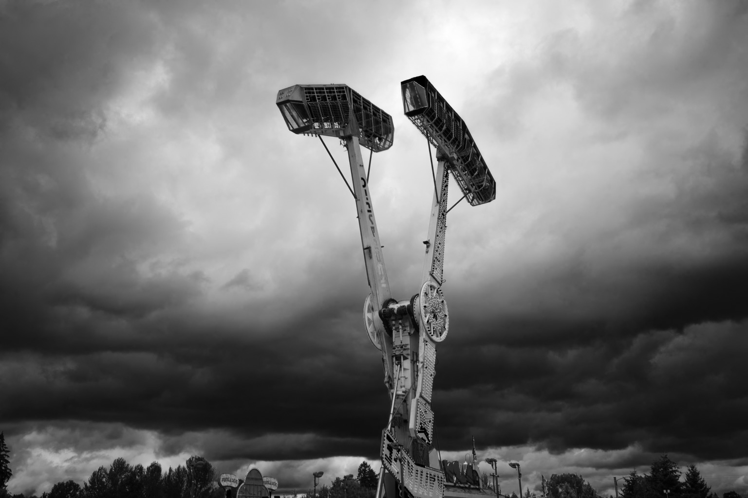 Monochrome image of a local carnival ride up in the air against ominous clouds.