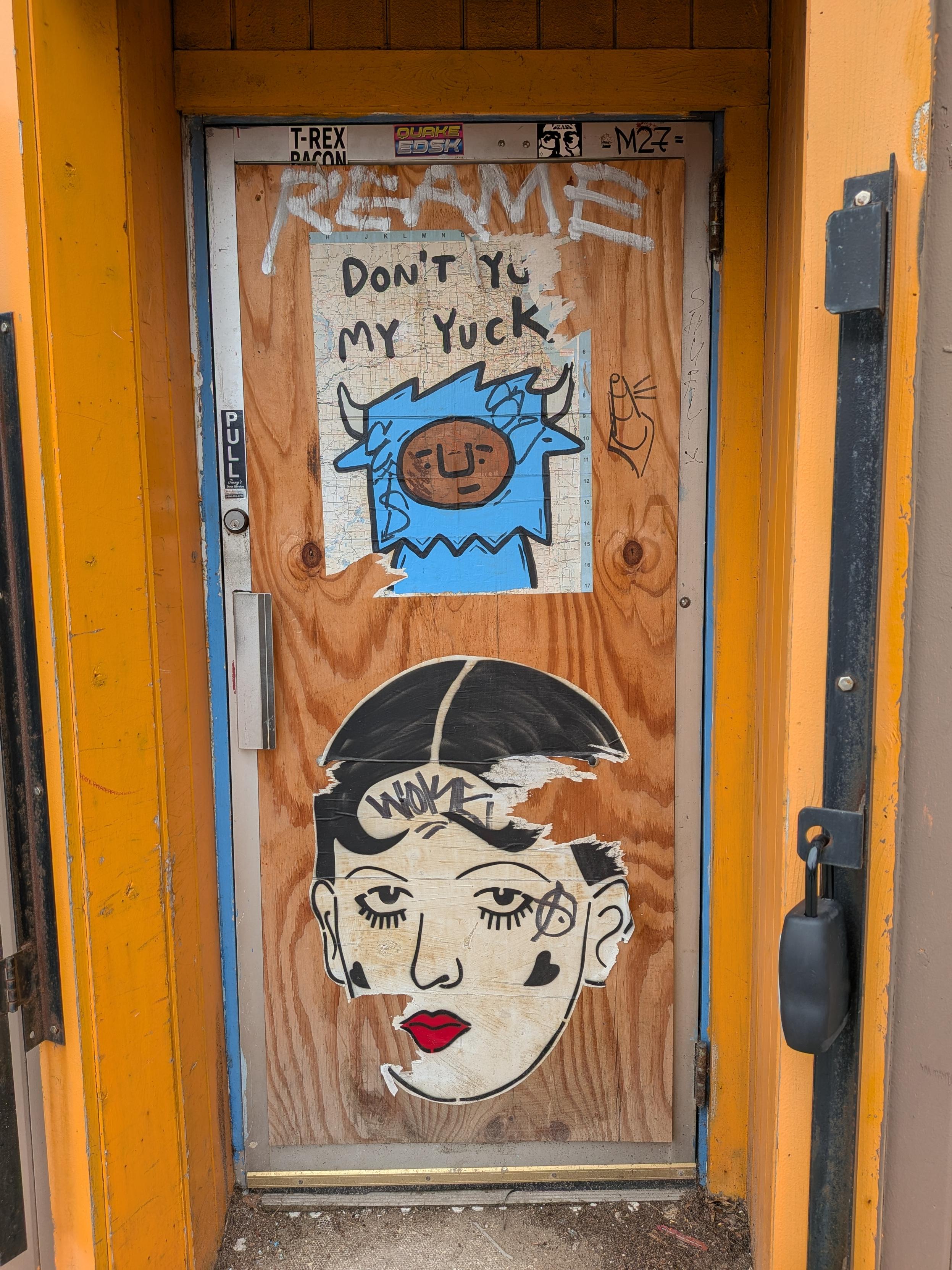 A digital photograph of an old wood door with metal frame covered in some graffiti. One bit of graffiti features a cartoon drawing of a yak or some cattle with the words "don't yu- my yuck" written above them, with yum cutoff.