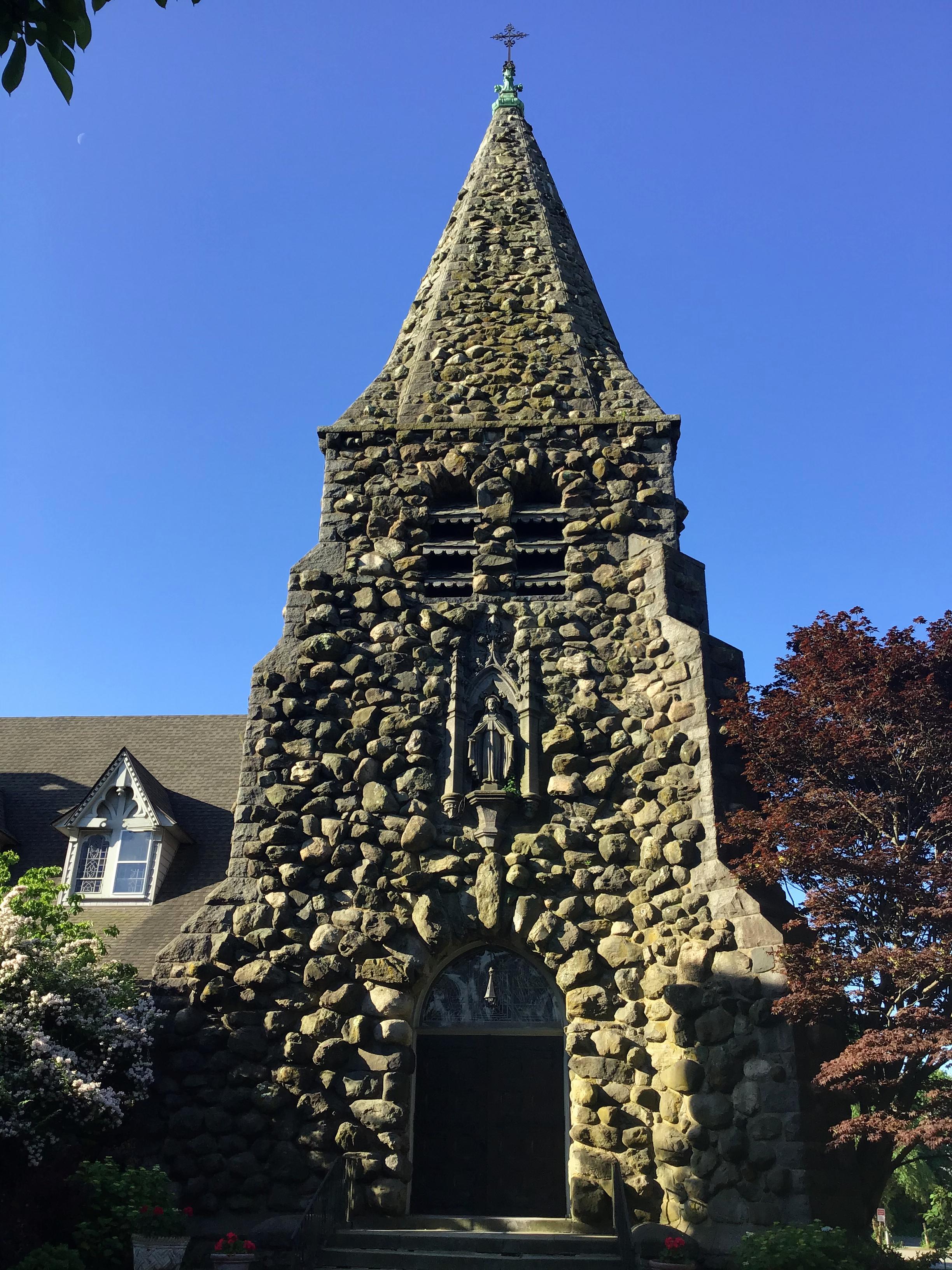 Entryway and steeple of an unusually-constructed church against a cloudless blue sky on a very sunny day.