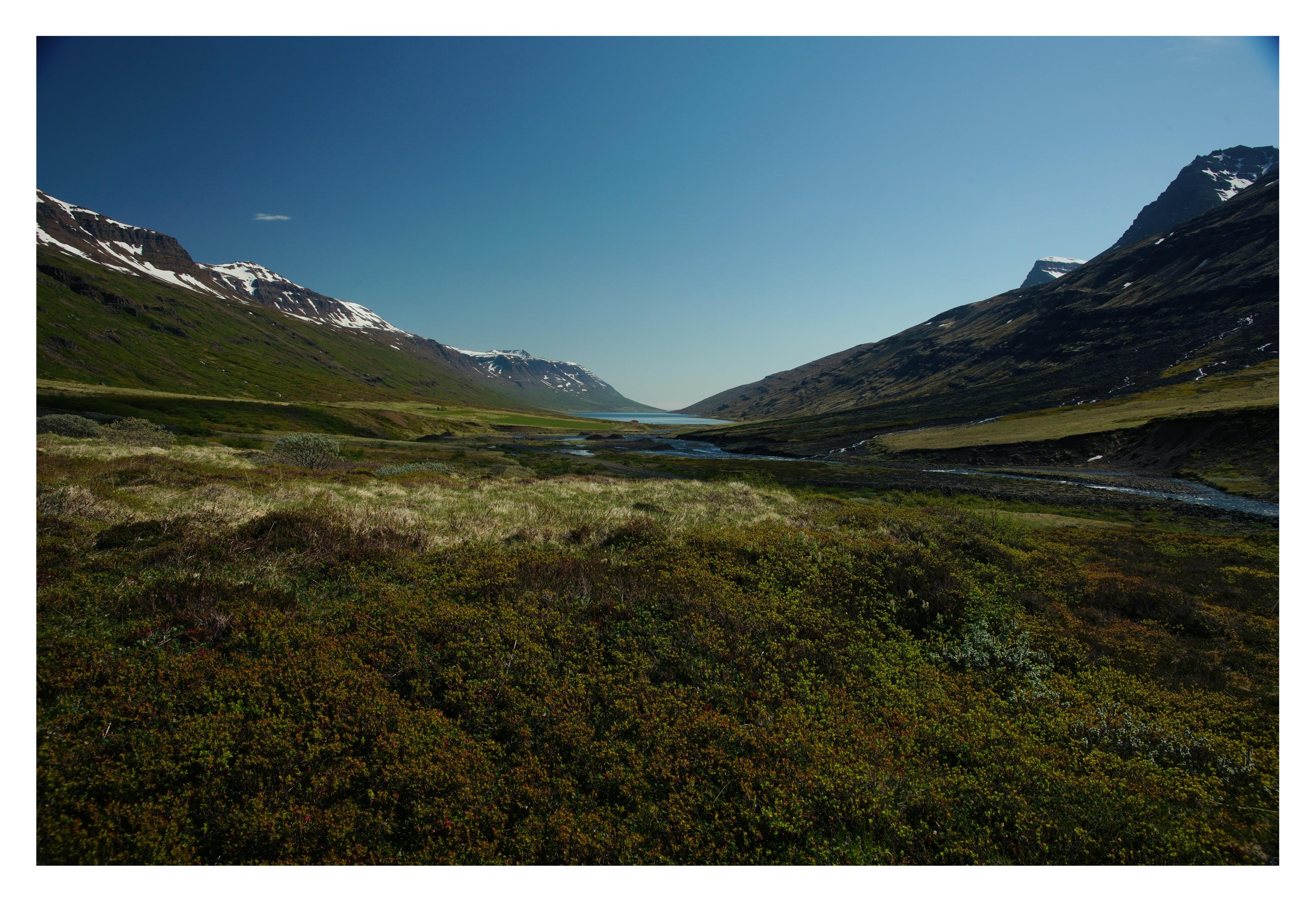 Ein Landschaftsbild. Rechts und links sind Berge mit Schneefeldern, von rechts kommt ein Fluss der in die Bucht führt und somit ins Meer :)