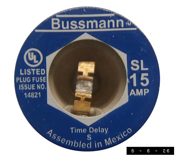 Old-style Bussmann 15-amp screw-in fuse for a vintage fuse box.  Blue metal with a clear window in the center showing the intact metal piece that burns and separates if too high a current flow is detected.  The famous "UL" in a circle emblem for Underwriters Laboratories appears on the left just above "LISTED PLUG FUSE ISSUE NO. 14821".  "Time Delay - S - Assembled in Mexico" appears near the bottom.  Measures about an inch and an eighth across.  A 15-amp fuse used to be standard for a typical household circuit.  Fuses with higher ratings might be used for the kitchen, laundry appliances, and the anti-alien ray gun cannons up on the roof.  Sometimes people would have one of these fuses pop and replace it with a penny instead of another fuse.  These people often became known as cremated remains.  Now we mostly use breakers that flip open when too much current is drawn.  You just flip them close when the problem has been solved.  Such breakers ended my childhood dream of spending my enti
