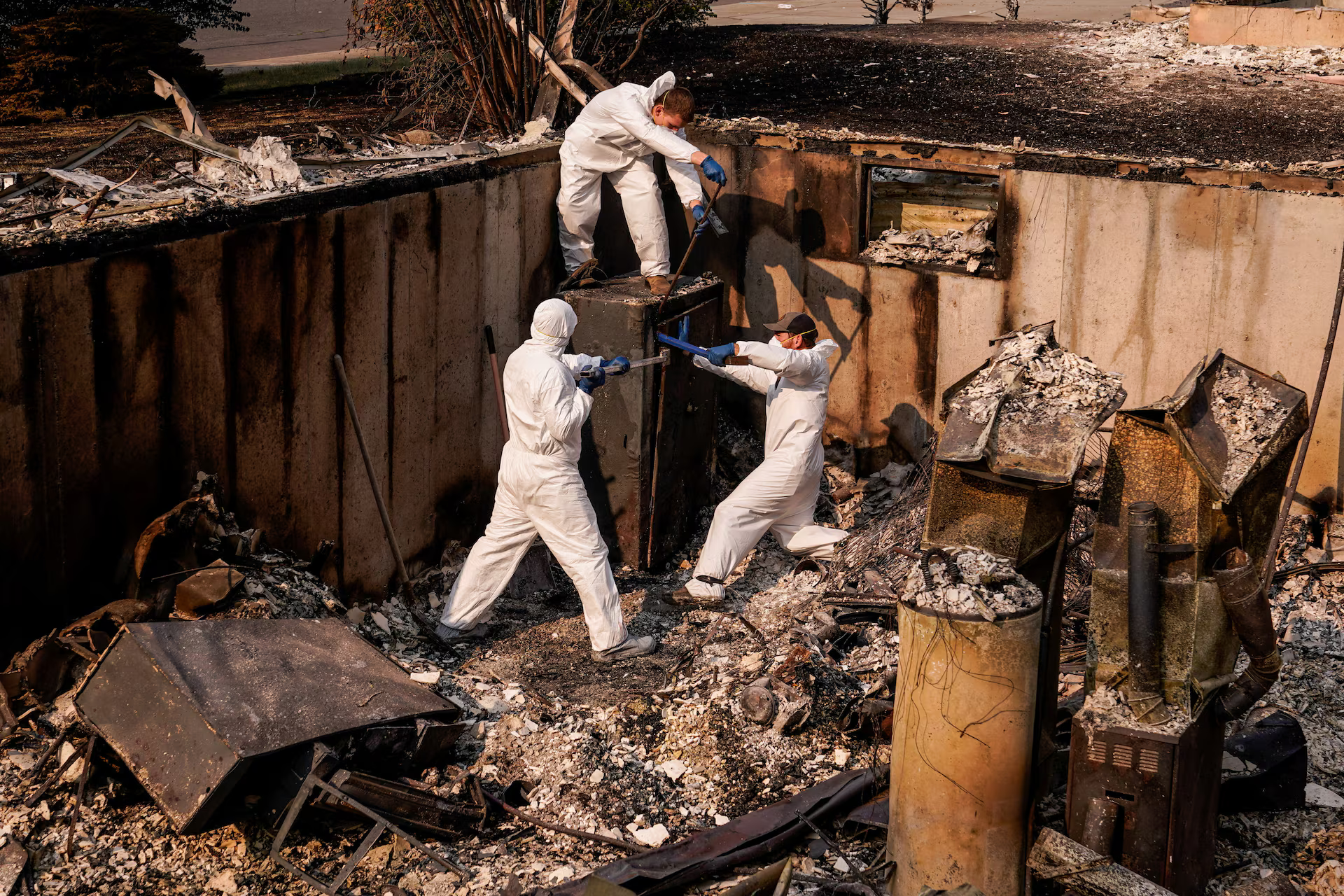 3 men in white protective gear try to crack open a safe.