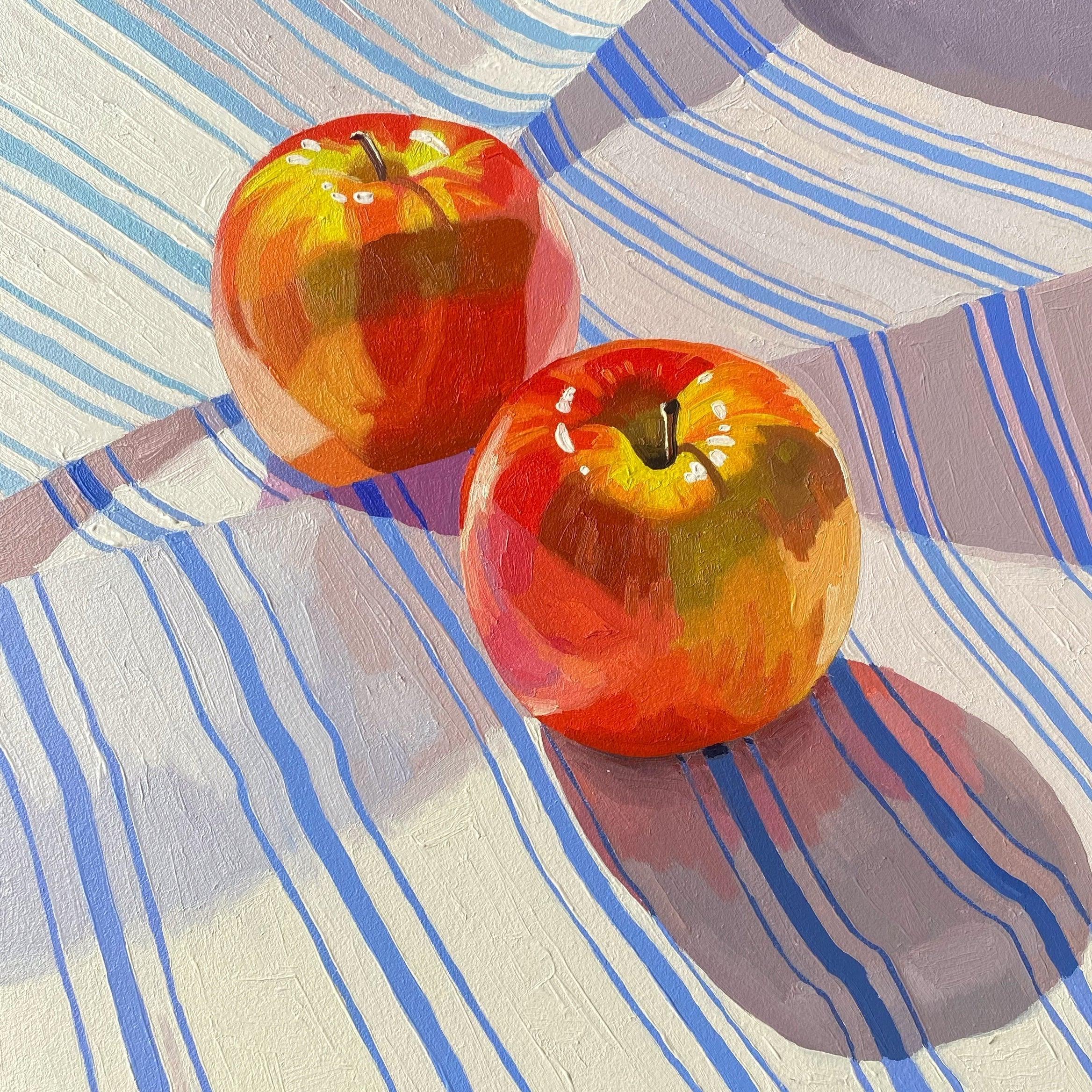 A still-life painting featuring two bright red apples placed on a light-colored striped cloth with blue lines. The apples cast soft shadows on the surface, highlighting their glossy texture and vibrant colors.