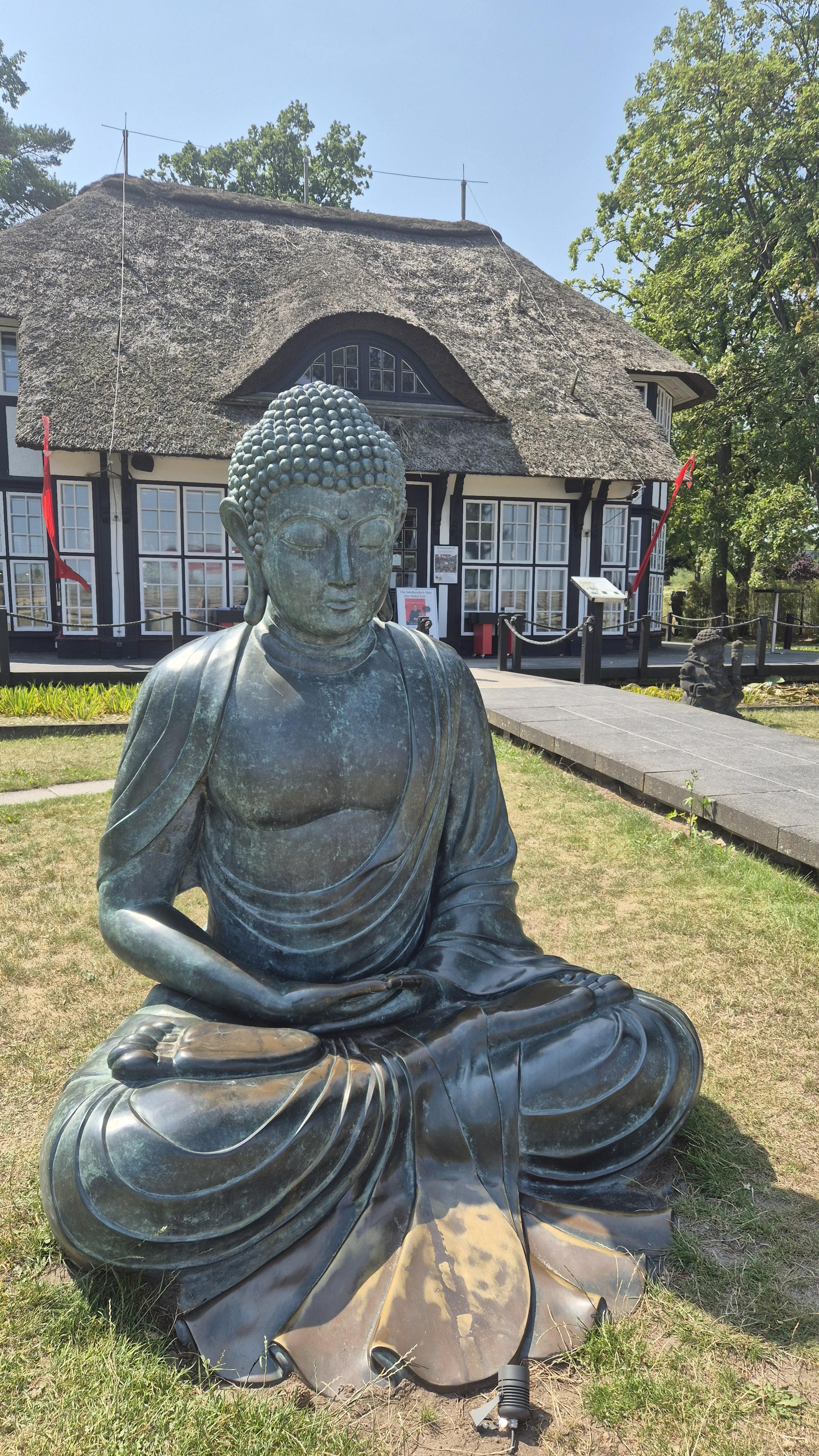 Sitzender Buddah vor einem japanischen Buchladen. /
A seated Buddha in front of a Japanese bookshop.
