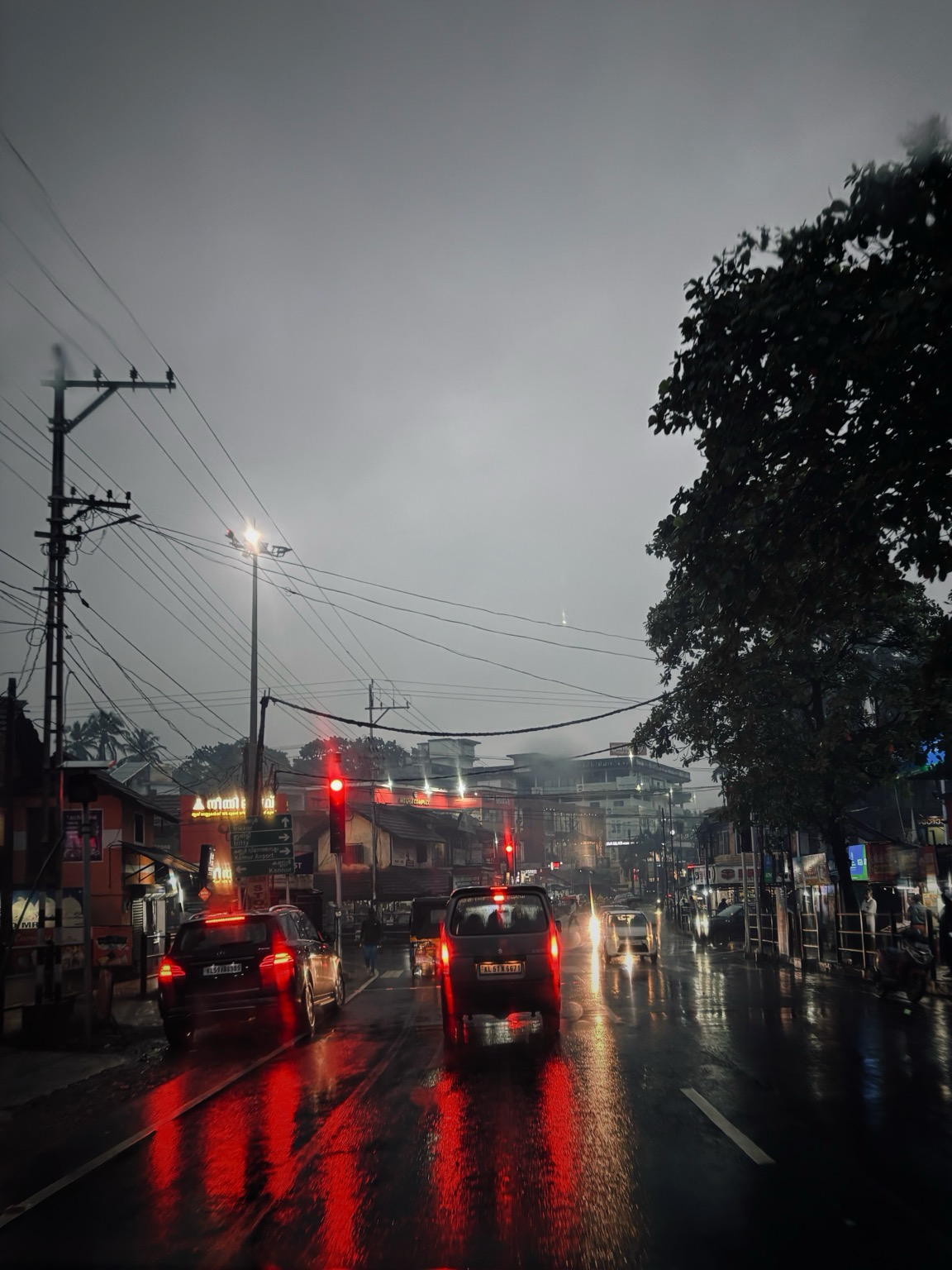 vehicles waiting at a traffic signal in a rainy evening.