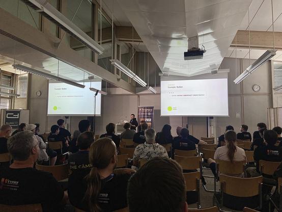 Kai Grosz on stage at TYPO3 Developer Days explaining the correct use of semantic HTML buttons for optimal accessibility.