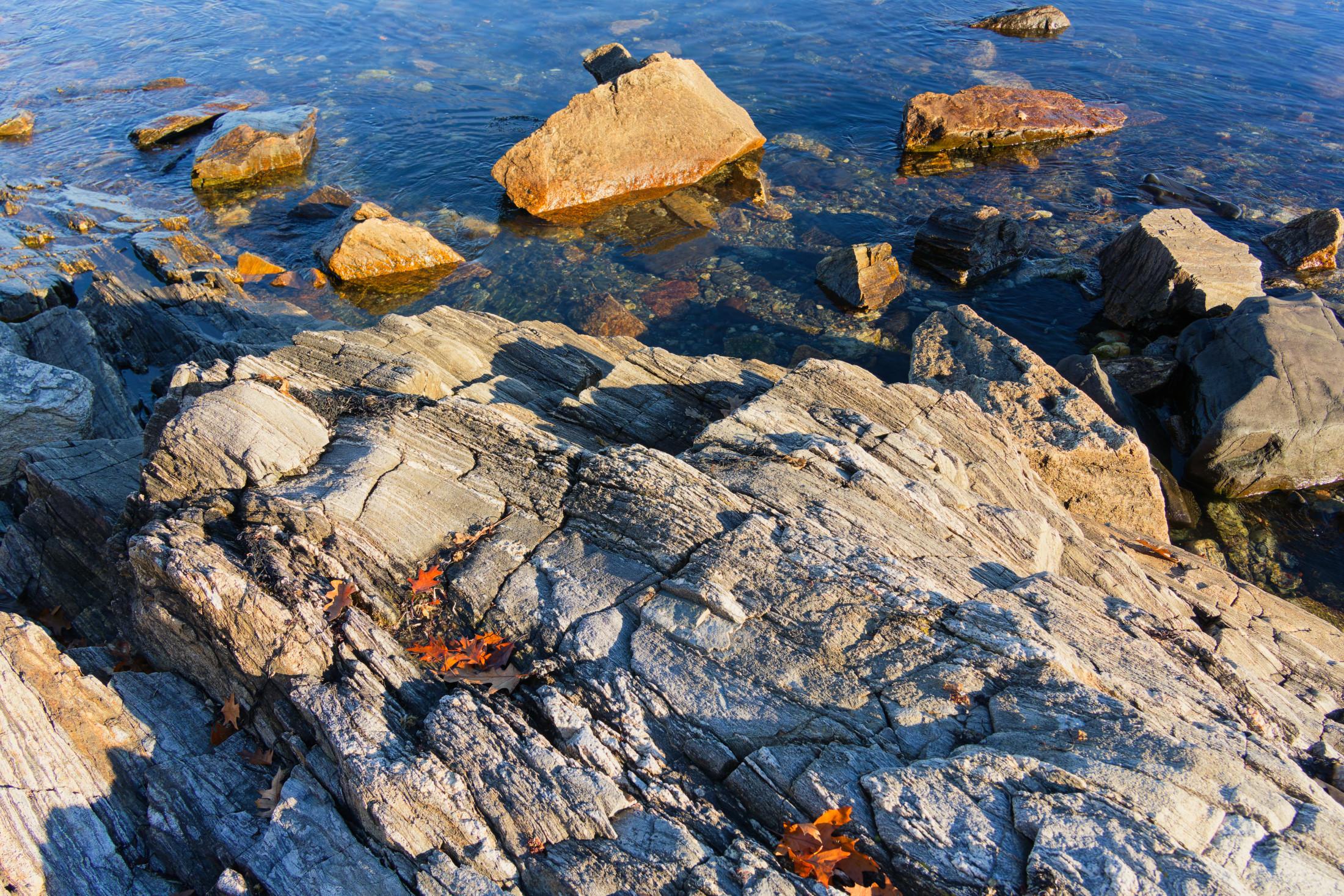 Some granite boulders resist weathering but others get etched by the action of waves and winds like the big one here on the New Hampshire store and others,  in the background are chunks of fill that were blasted and transported by truck!
