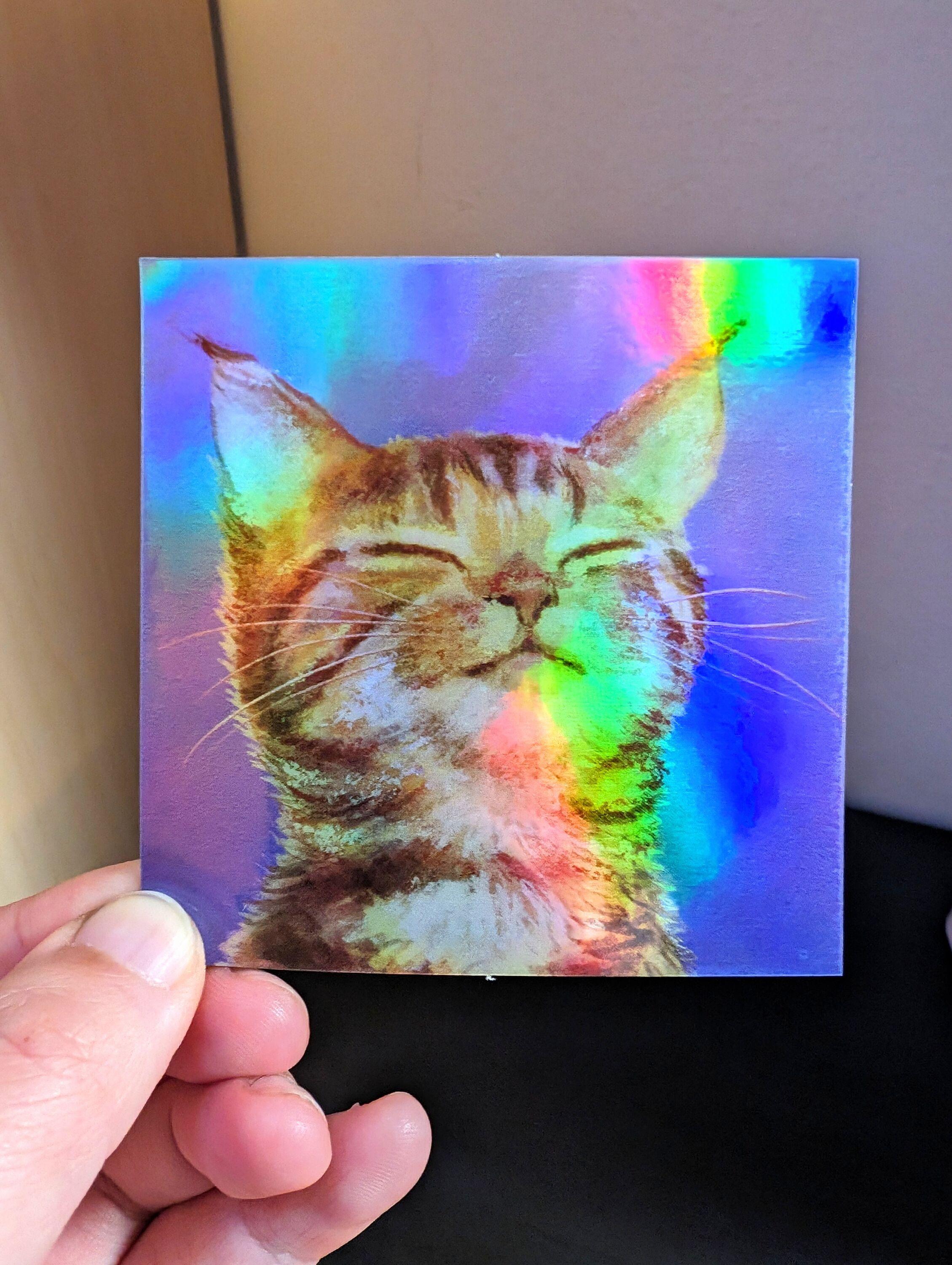 Photo of a left hand holding a square sticker. The sticker is a holographic painting of a content orange cat.