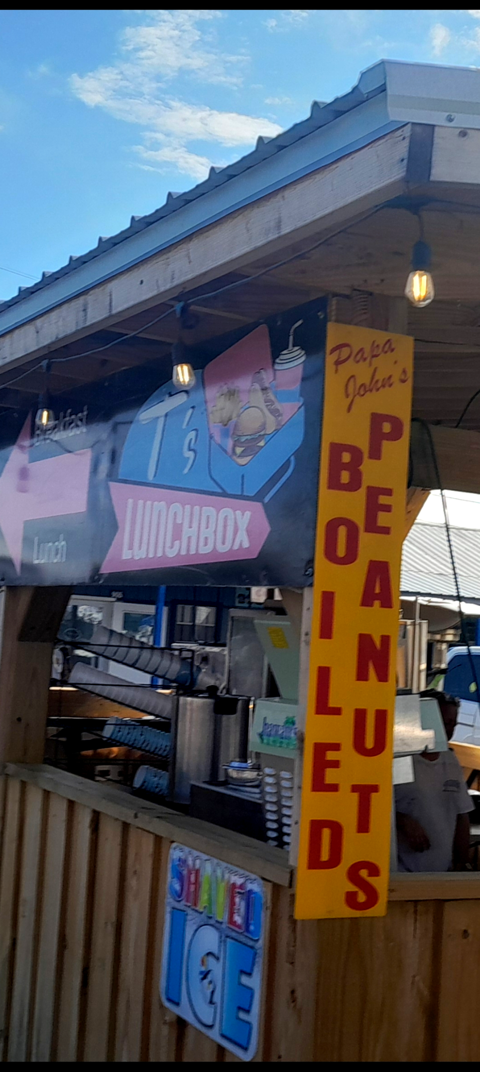 Many multicolor signs including red Boiled Peanuts on a yellow background and T's Lunchbox on a food vendor spot at the flea market