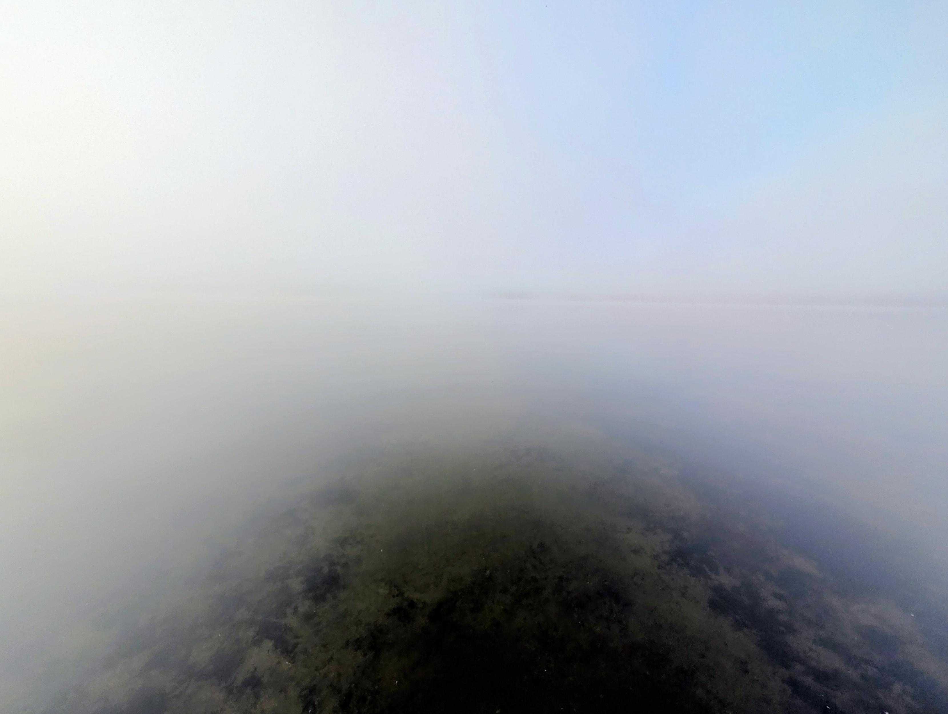Lac Simon perdido en la niebla. Se observan algunas algas en el lago.