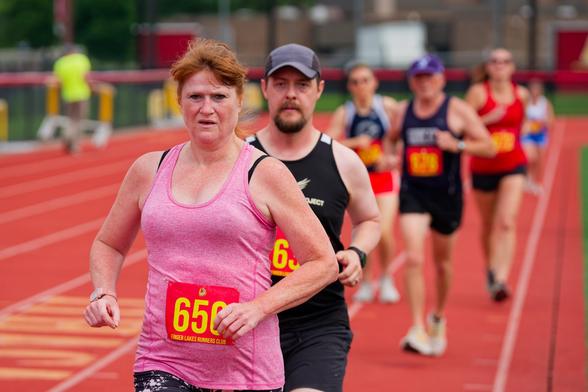 A woman in pink and a man in black lead a group of runners down a red track