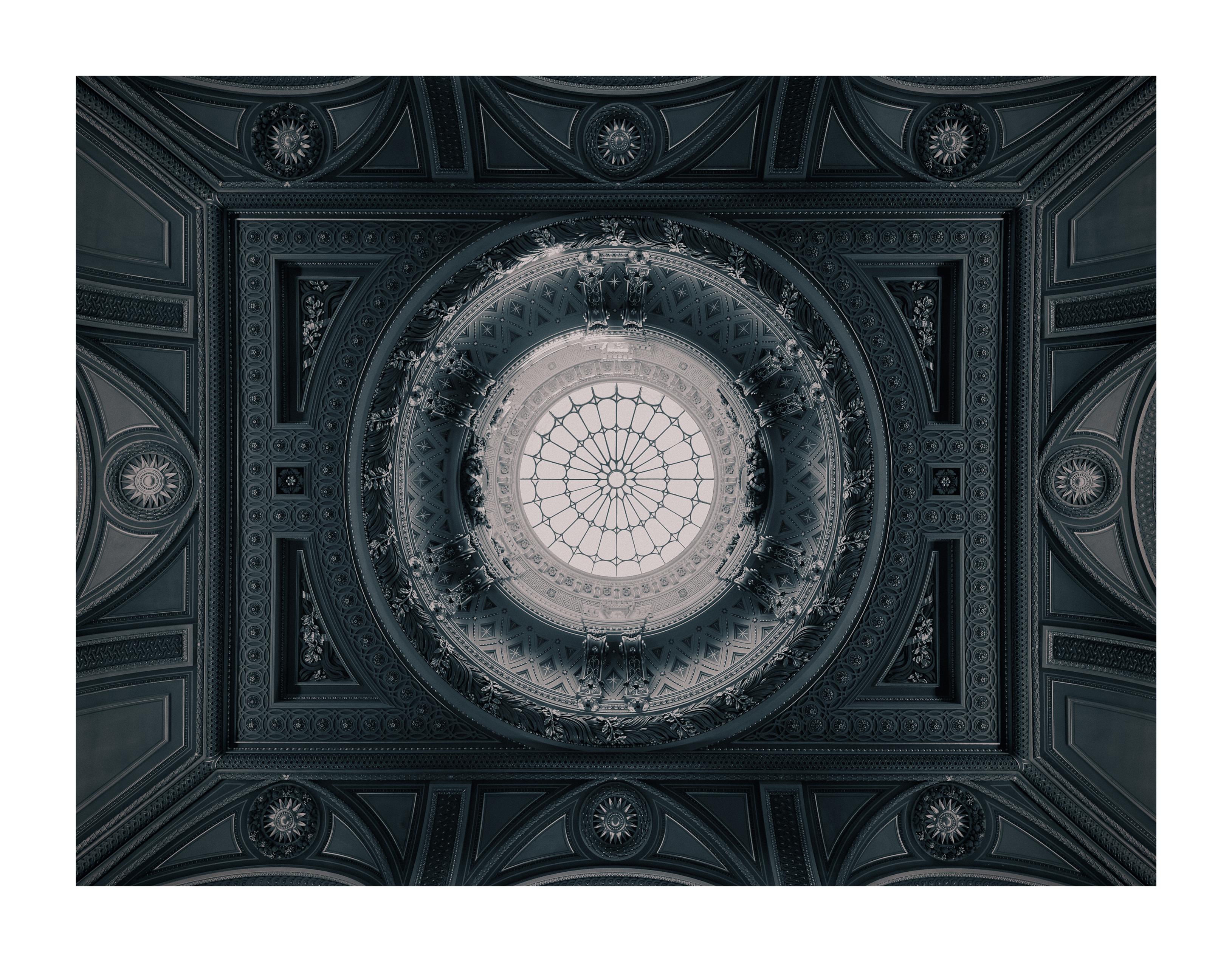An ornate, symmetrical ceiling looking directly up at a glass dome in the centre. Although it has a golden colour in real life, the edit gives the image a blue monochrome appearance.